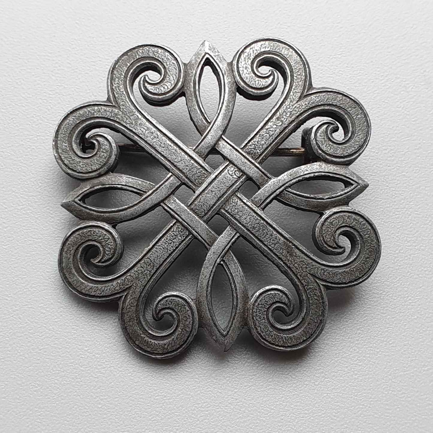 Ornate metal brooch or pendant with an intricate Celtic knot design featuring spirals and interwoven patterns.