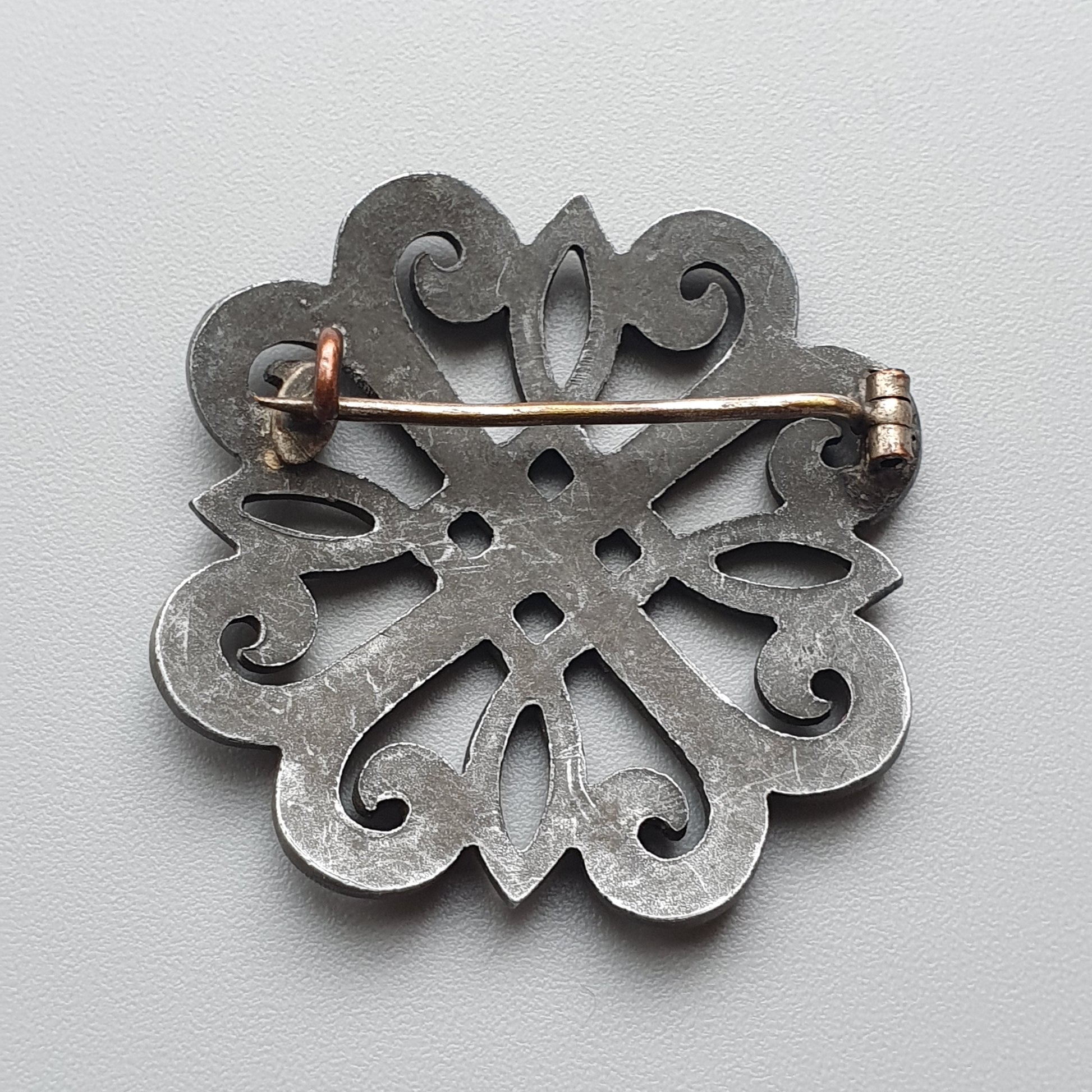 Ornate metal brooch with a floral or snowflake-like design featuring intricate cutouts and swirling patterns.