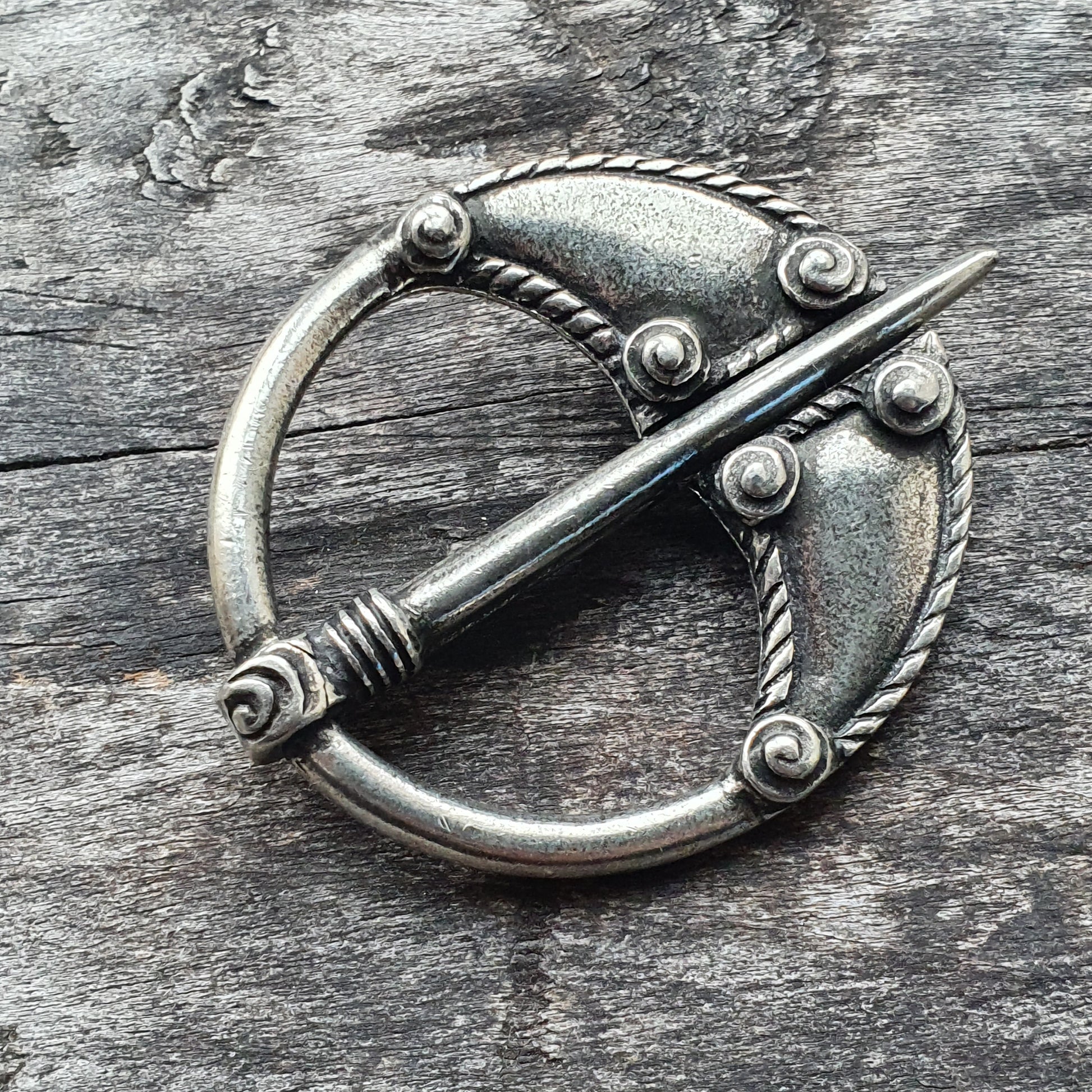 Ornate silver brooch with a circular design and decorative pin.