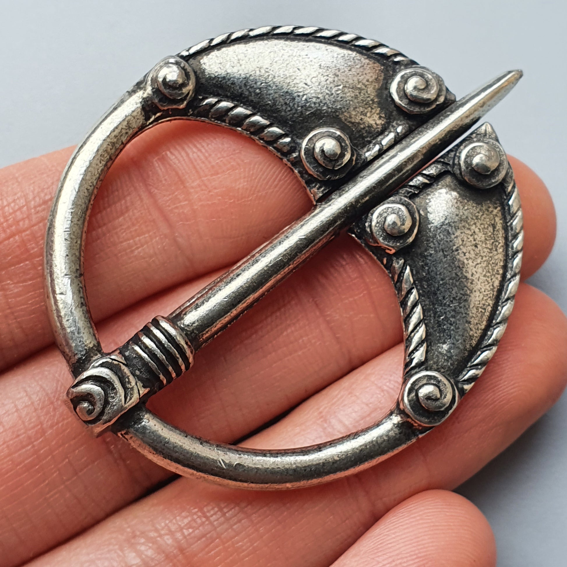 Ornate silver circular brooch with a decorative pin across its center.