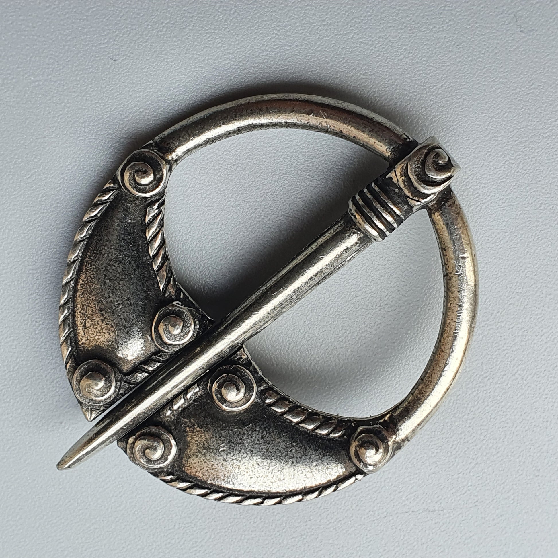 Ornate silver circular brooch with a decorative pin across its center.