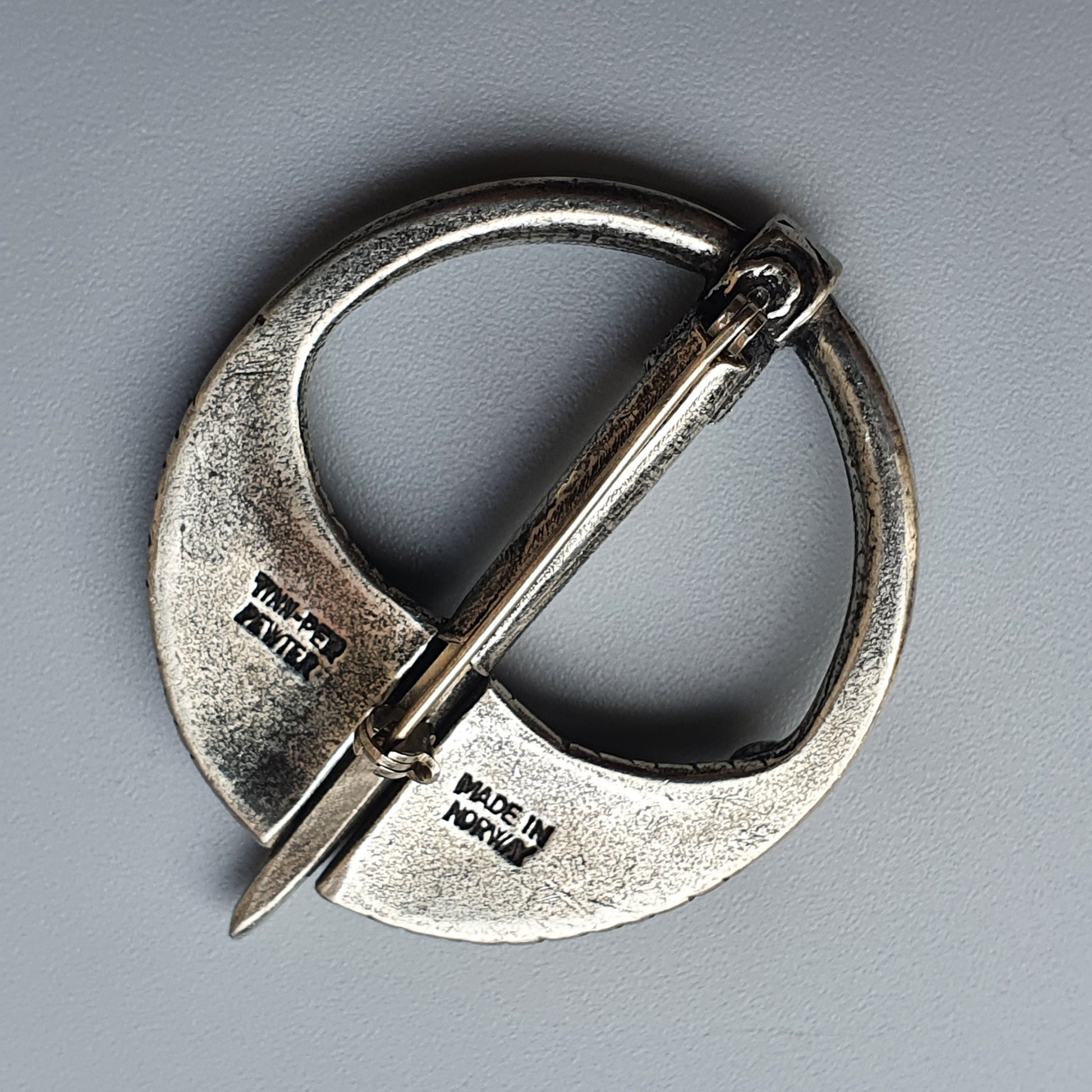 Silver circular brooch or penannular fibula with a pin across its opening.