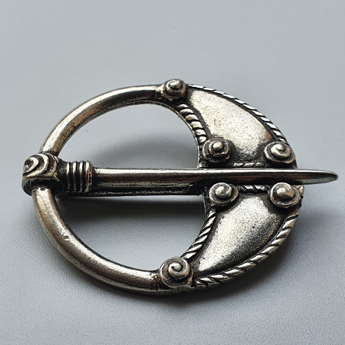 Ornate silver brooch or cloak pin with a circular design and decorative elements.