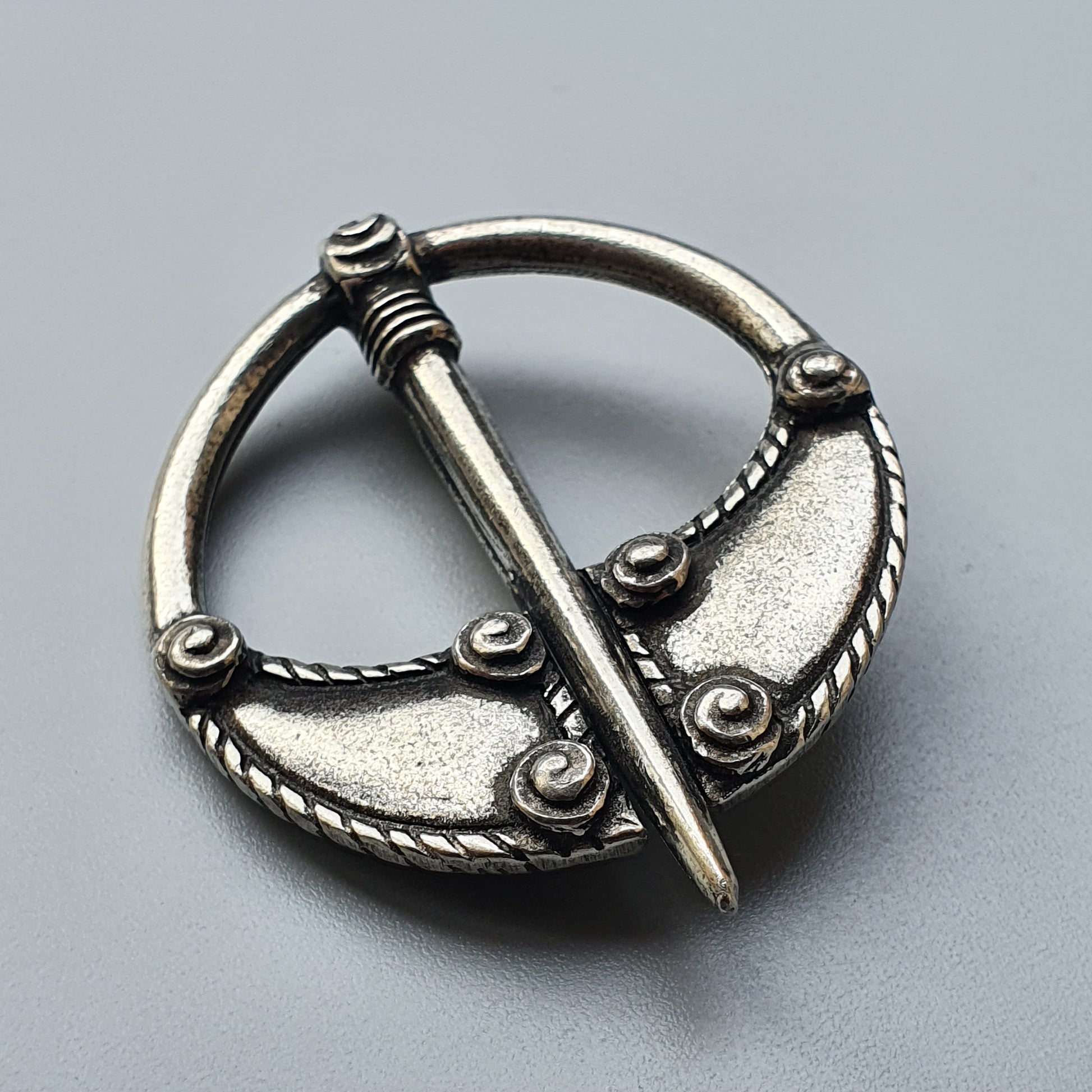 Ornate silver penannular brooch with decorative rope-like patterns and a pin.