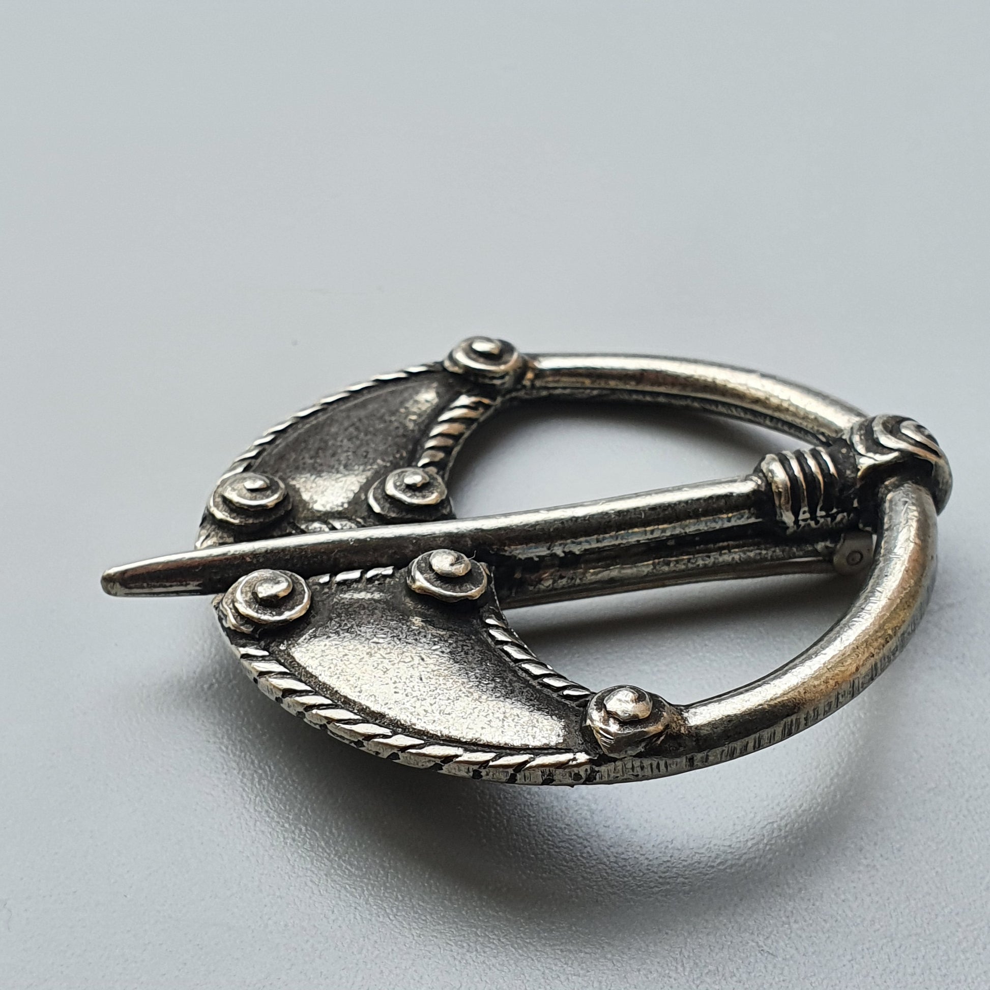 Ornate silver brooch or cloak pin with a circular design and decorative details.