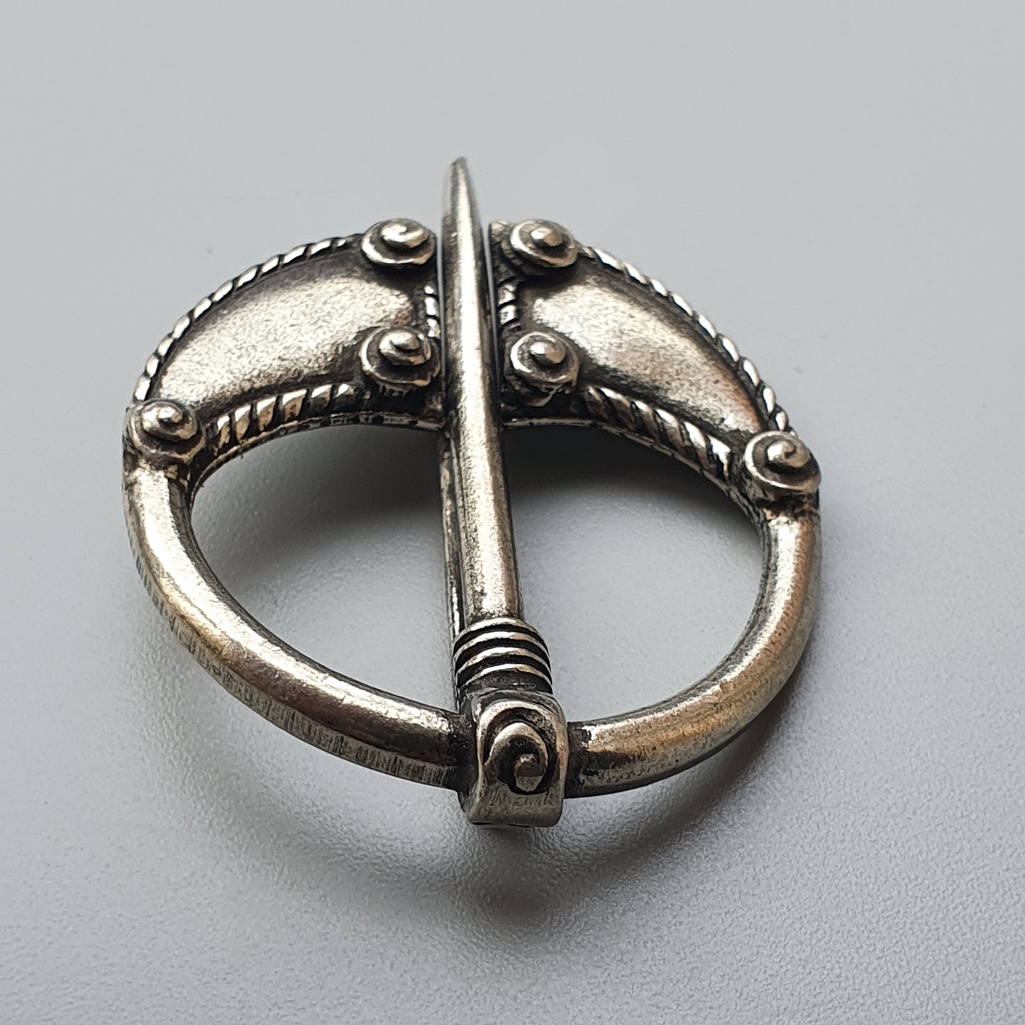 Ornate silver brooch with a central pin and decorative studs along its circular frame.