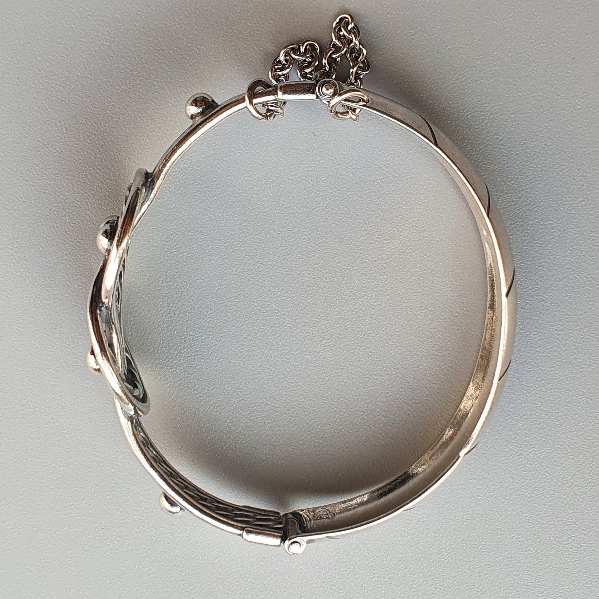 Silver bracelet with ornate floral or vine-like decorative elements.