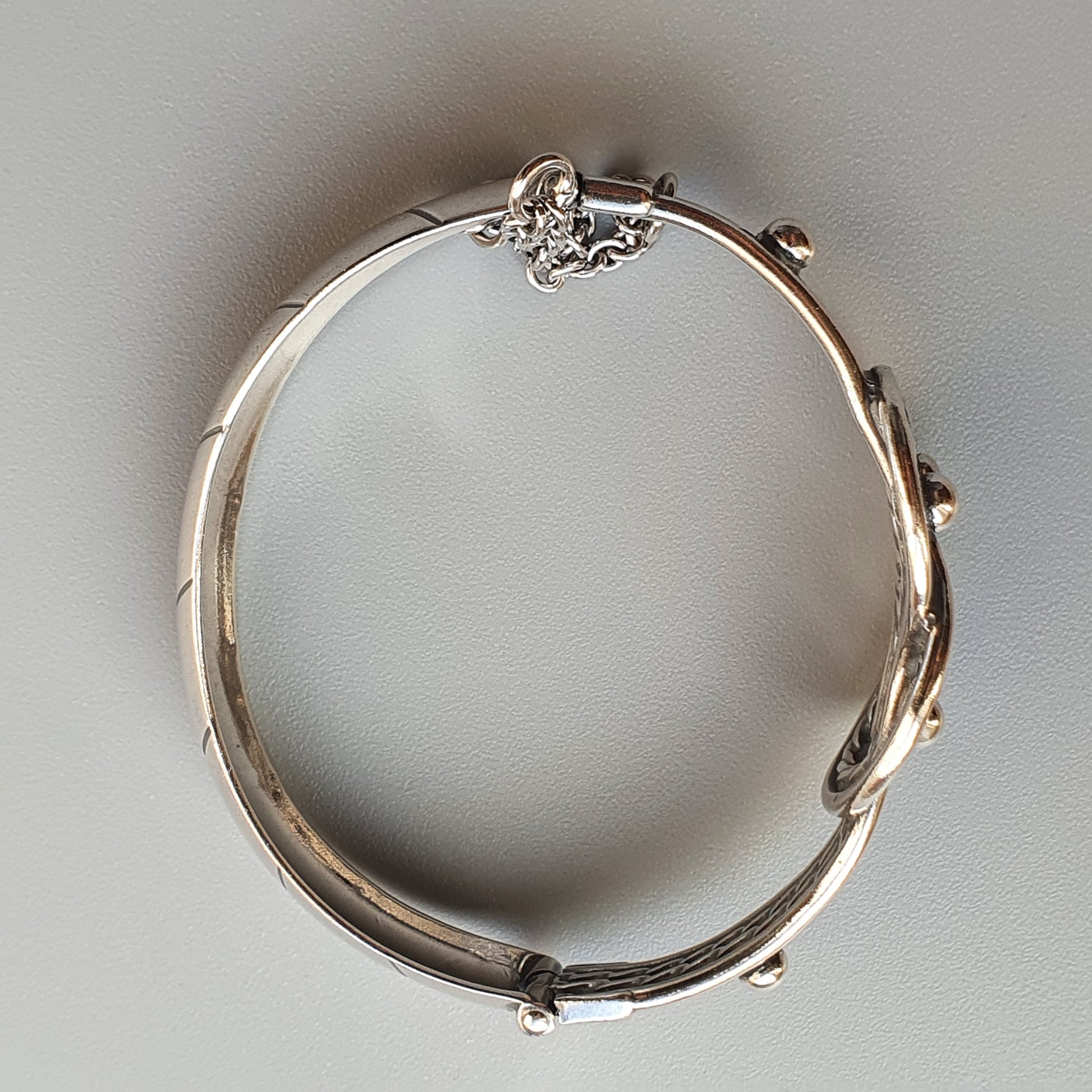 Silver bracelet with decorative floral or leaf-like elements along its band.