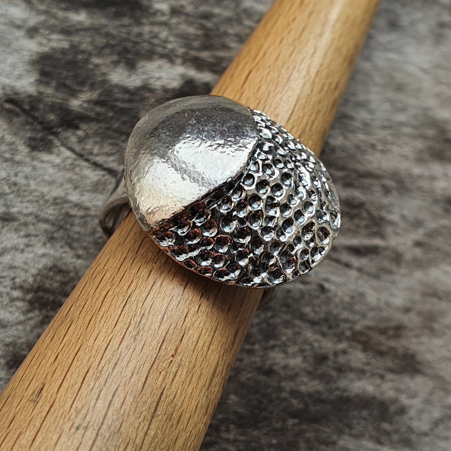 Silver ring with a textured, dome-shaped design resting on a wooden surface.