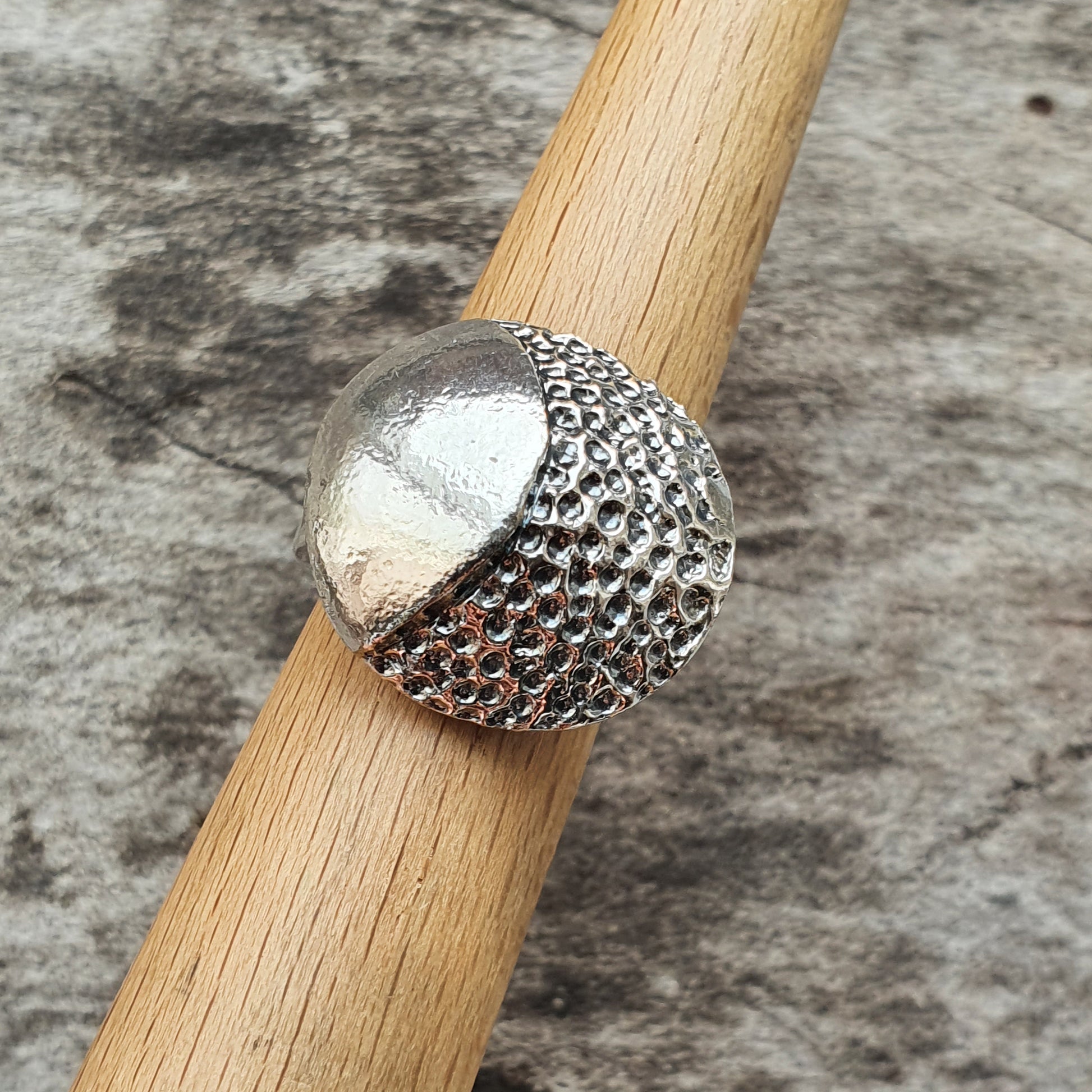 Silver ring with a textured, dome-shaped design on a wooden surface.