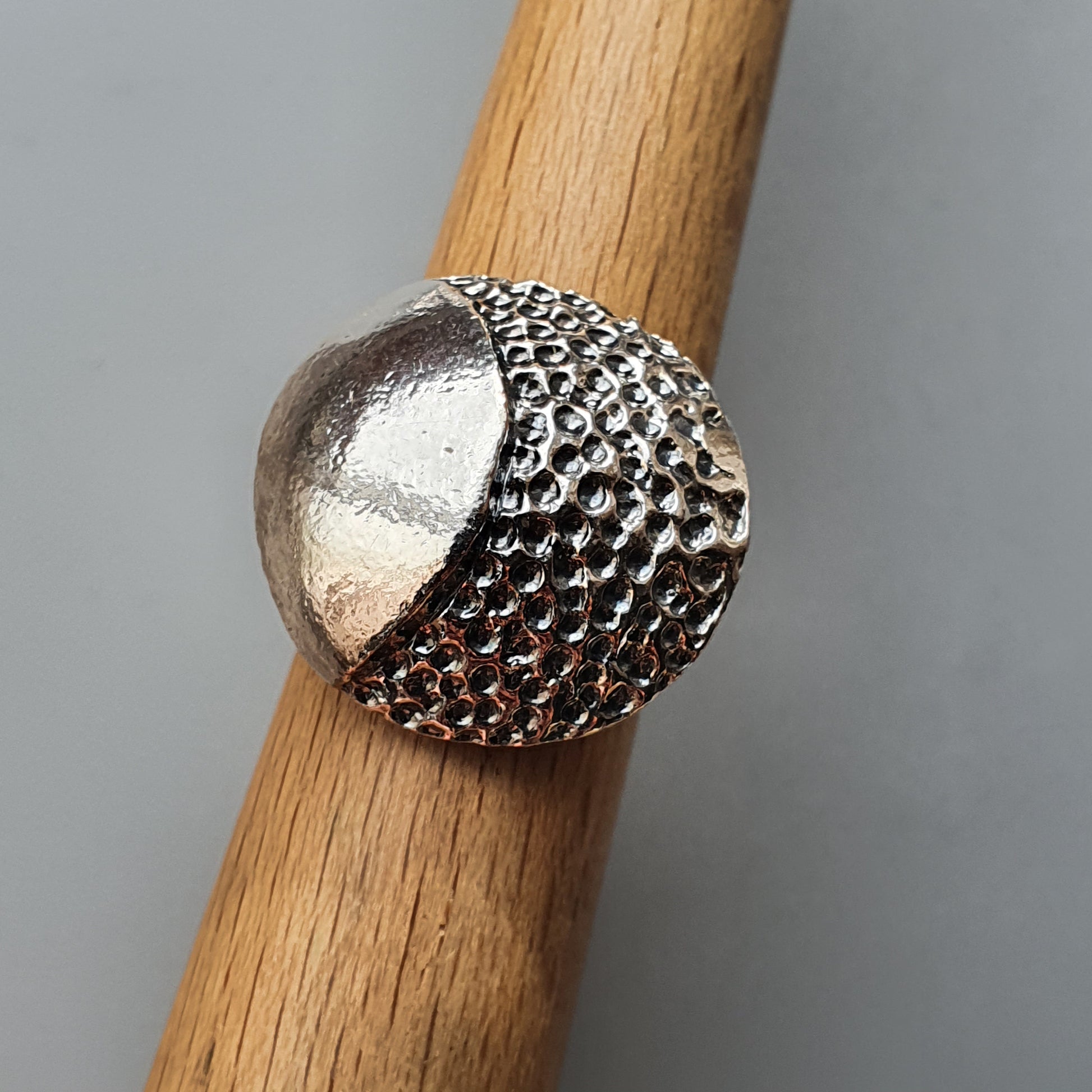 Silver ring with a textured, dome-shaped design on a wooden surface.