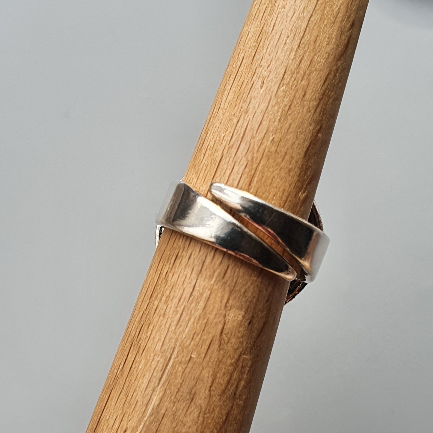 Silver ring with a split design wrapped around a wooden dowel.