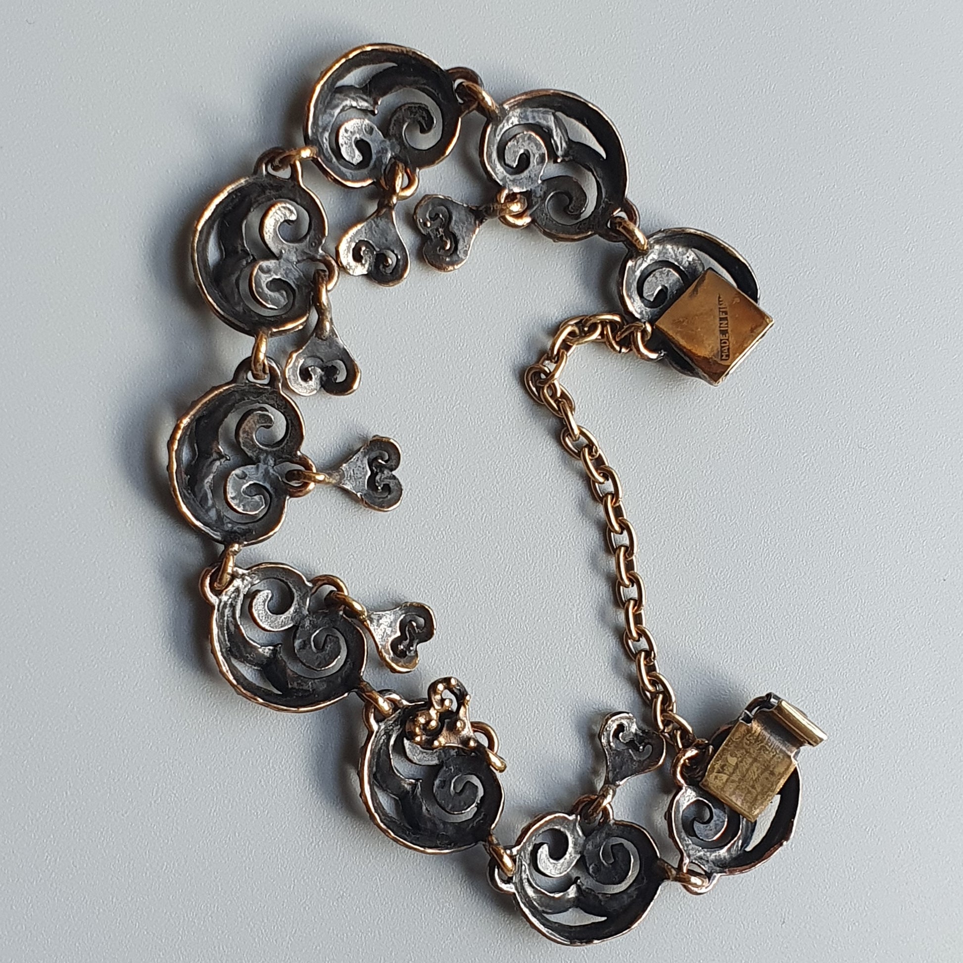 Ornate silver and gold bracelet with swirling scroll designs and heart shapes.