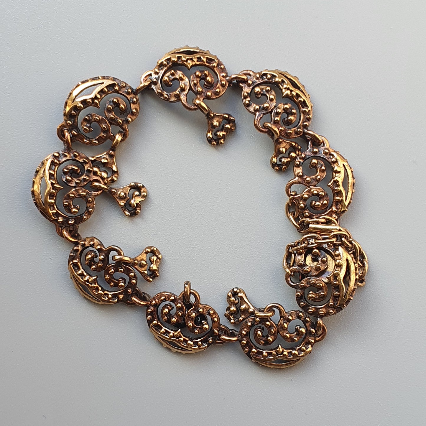 Ornate gold-toned bracelet with intricate filigree designs forming circular links.