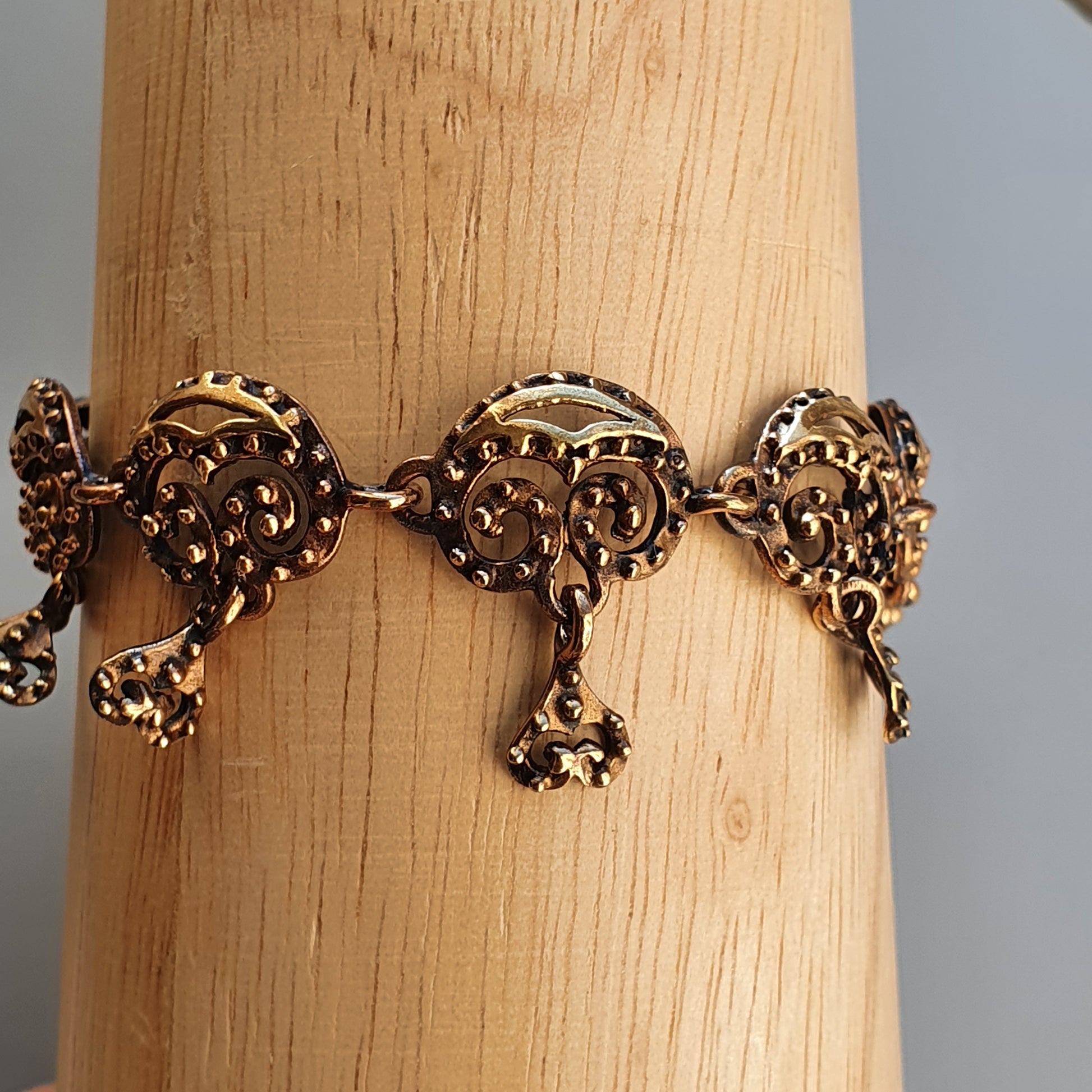 Ornate gold-toned bracelet with intricate filigree designs and dangling charms.