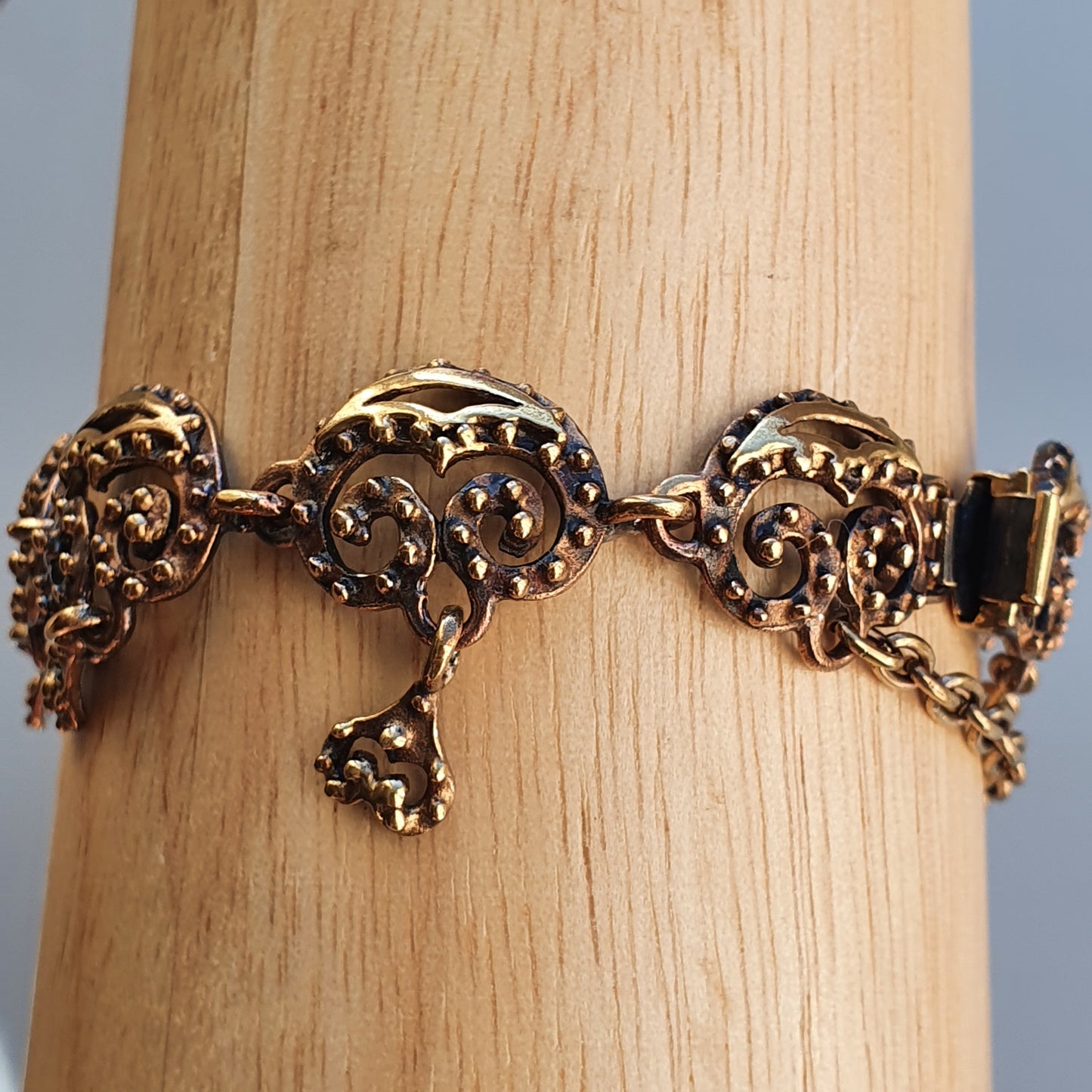 Ornate gold-toned bracelet with intricate filigree designs and dangling elements.