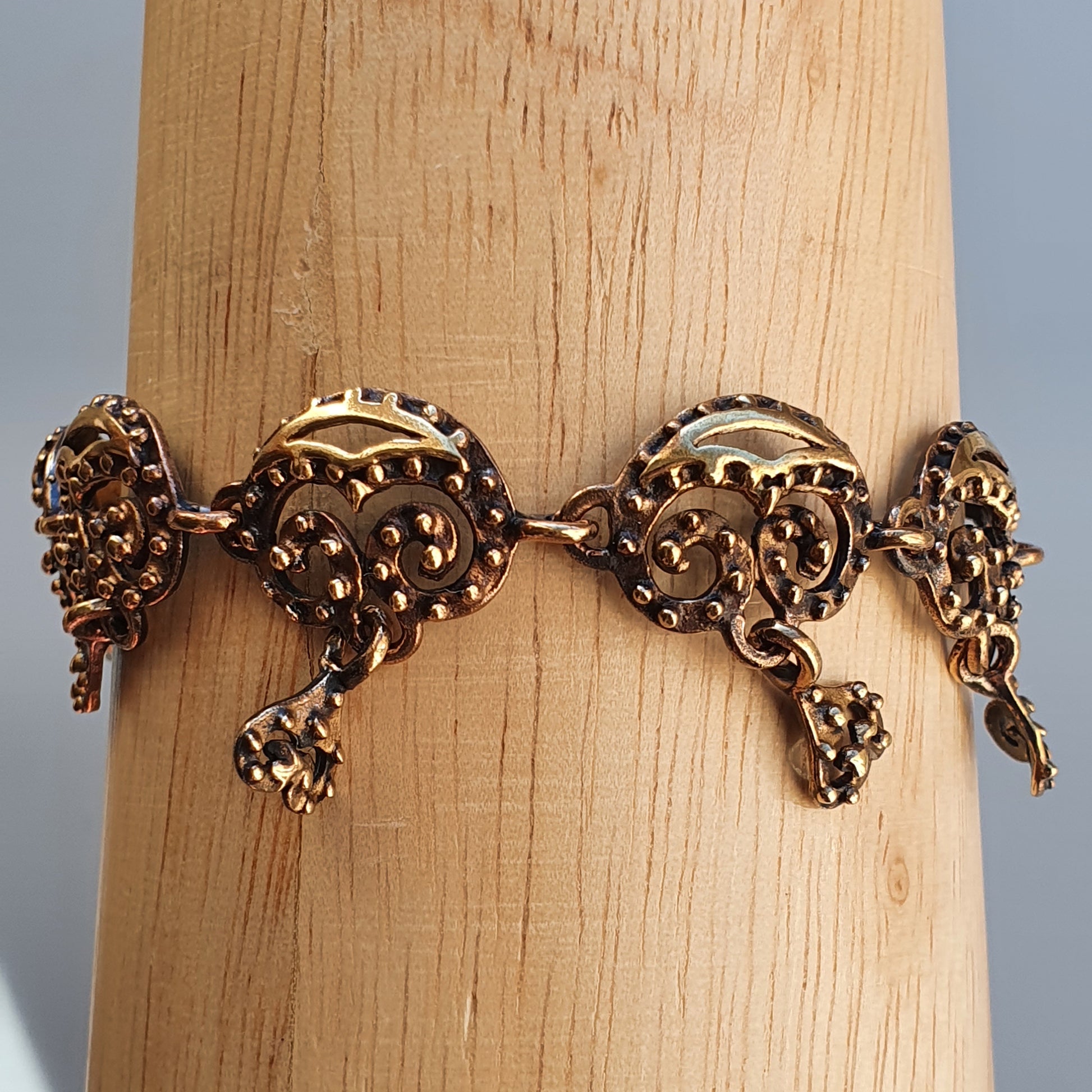 Ornate gold-toned bracelet with intricate filigree designs and dangling elements.