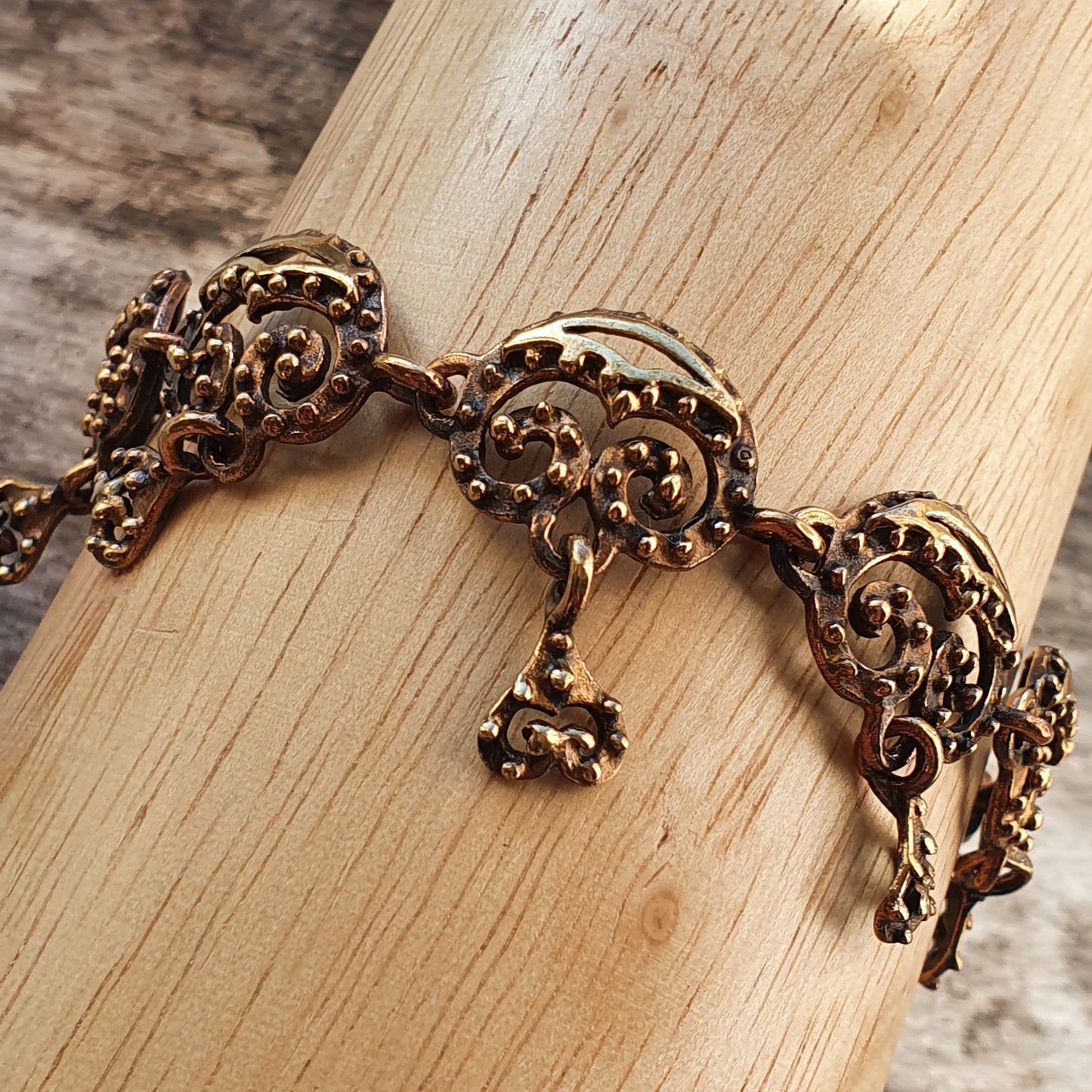 Ornate gold-toned metal bracelet with intricate filigree designs and a dangling charm.