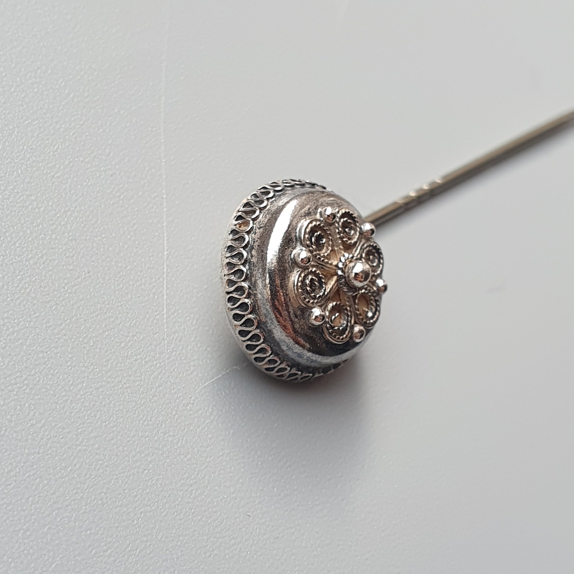 Ornate silver hatpin with a decorative round head featuring floral or star-like patterns.