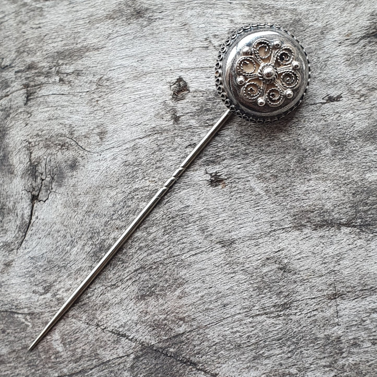 Ornate silver brooch or pin with a circular decorative head and long needle-like stem.