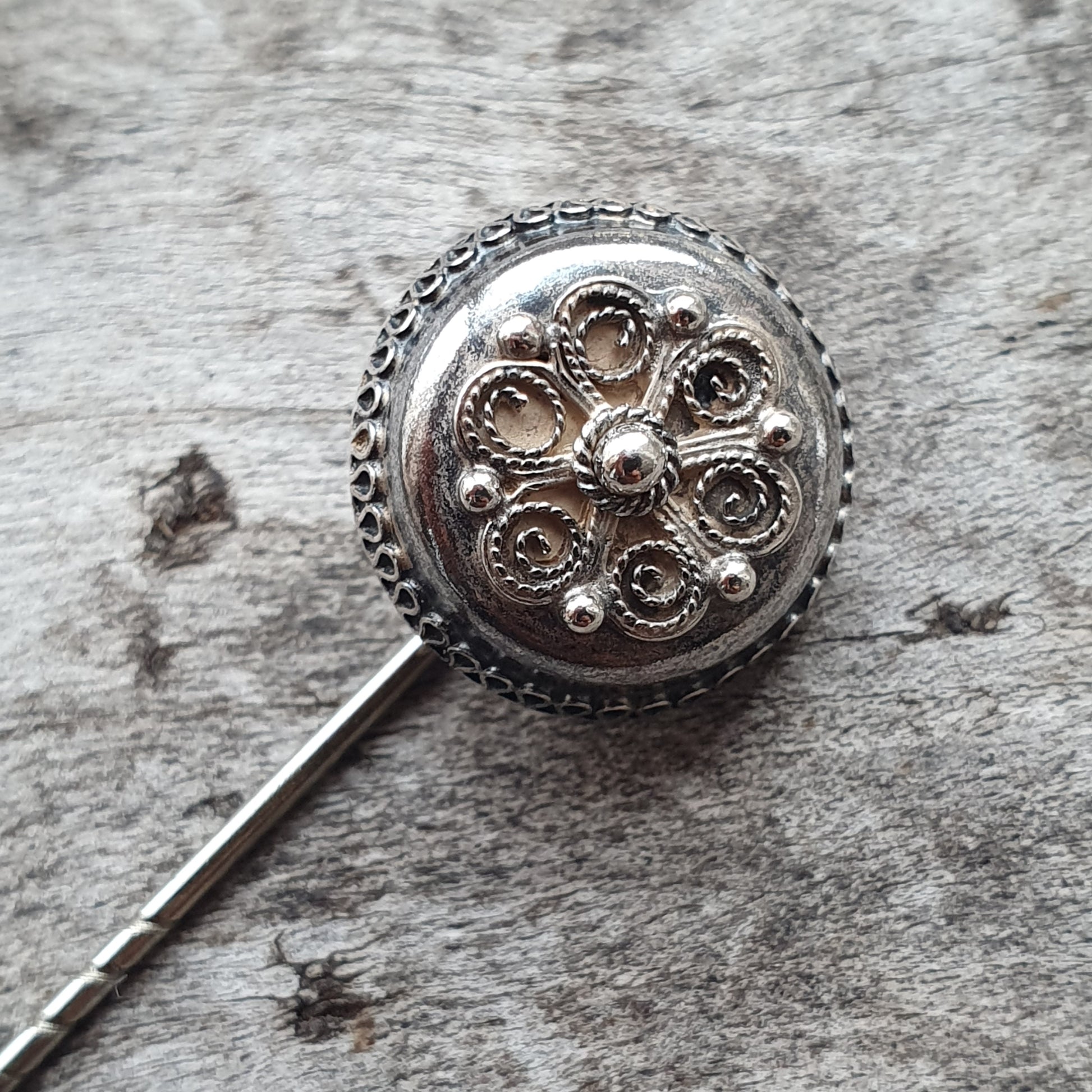 Ornate silver brooch or pin with a circular floral design.