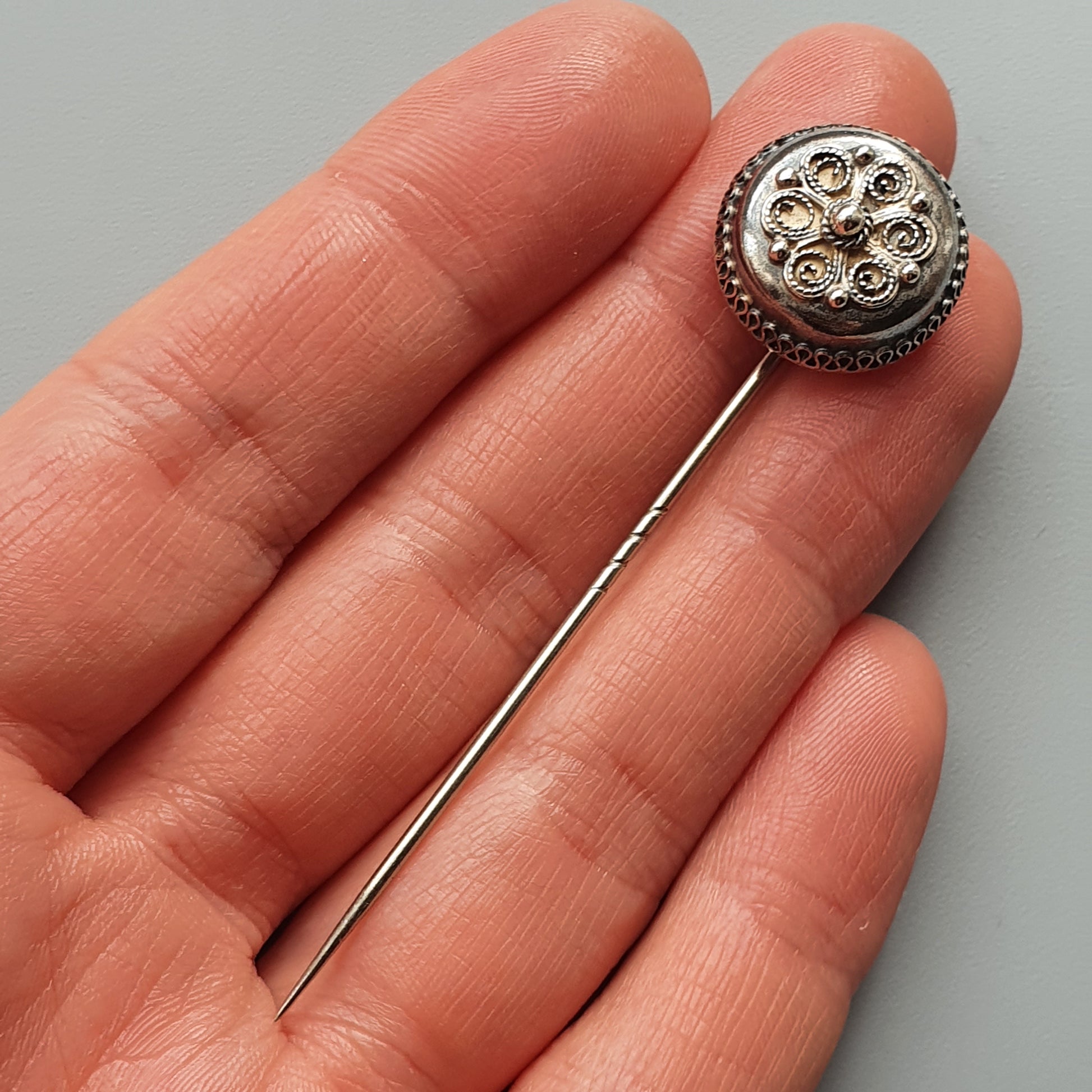 Ornate silver stick pin with a circular filigree design on its head.