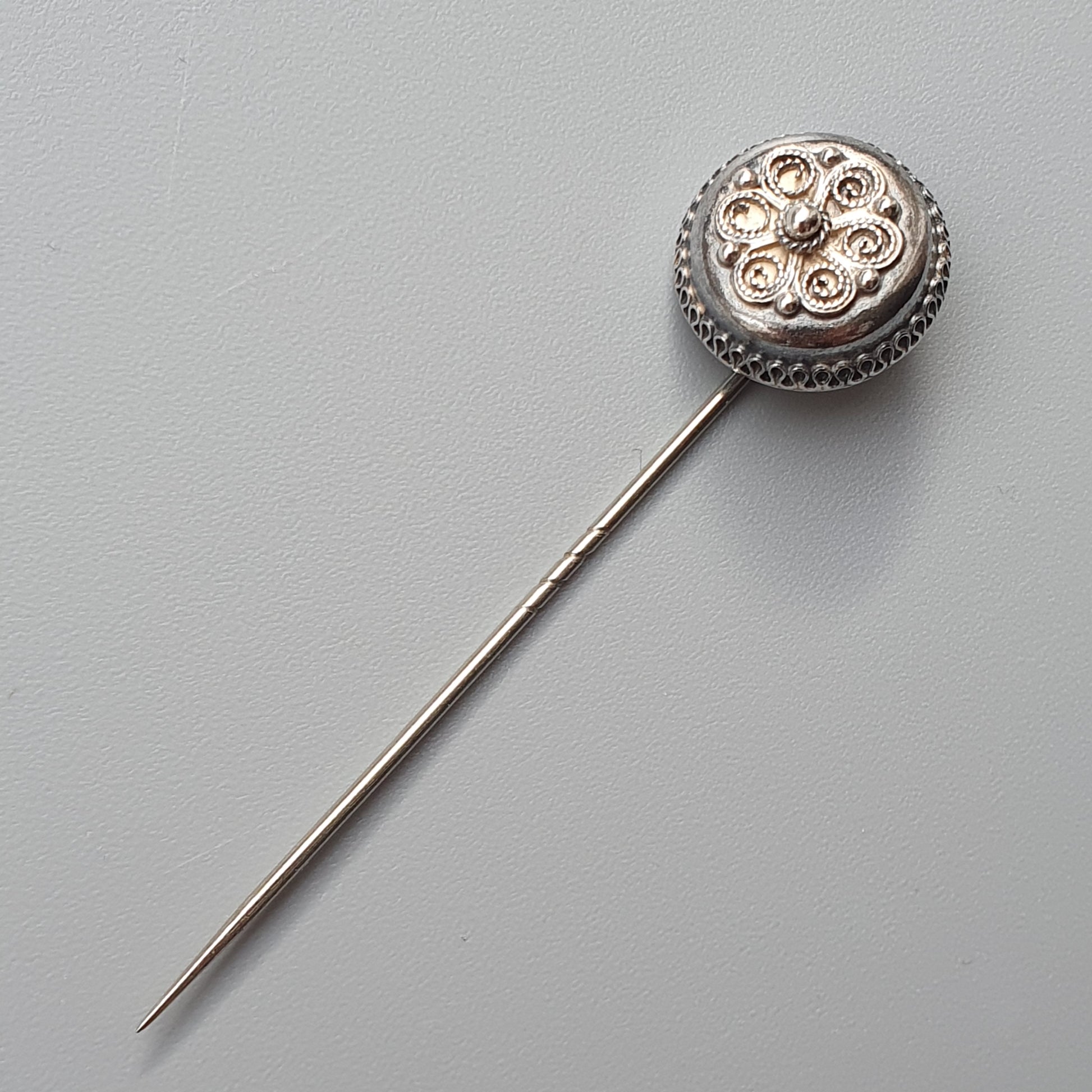 Ornate silver hatpin with a decorative round head featuring floral designs.