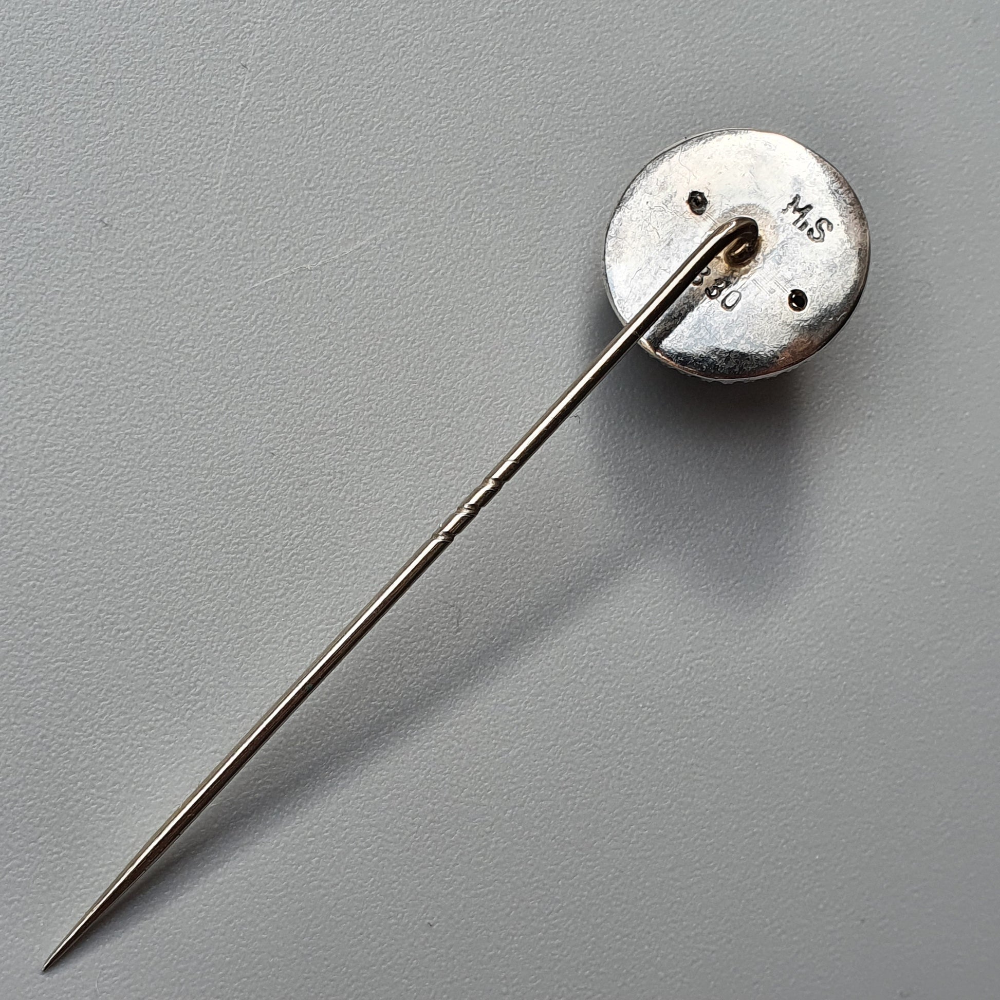 Silver lapel pin with a long needle and circular head marked ’145’’.