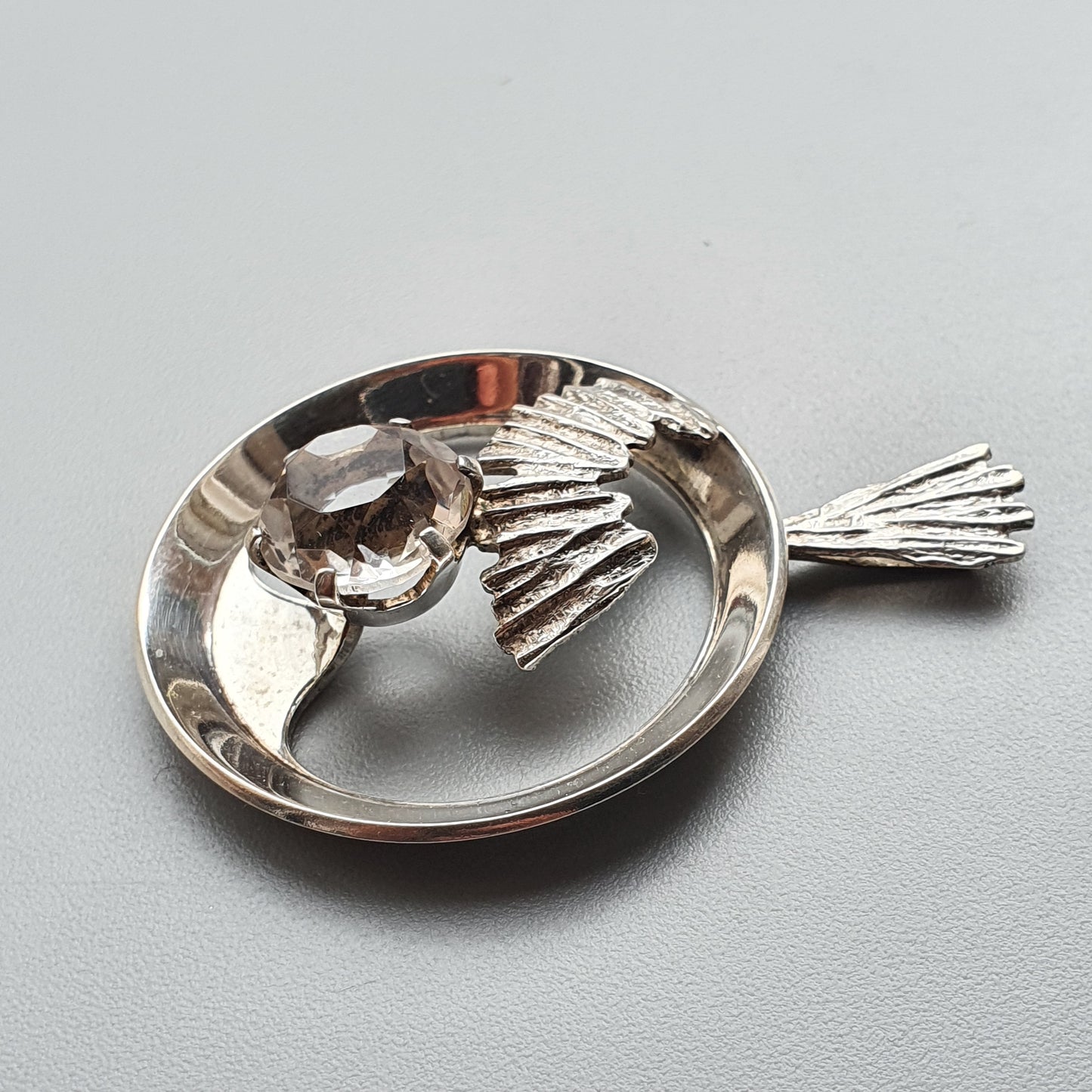 Silver brooch or pendant shaped like a stylized fish with a gemstone eye.