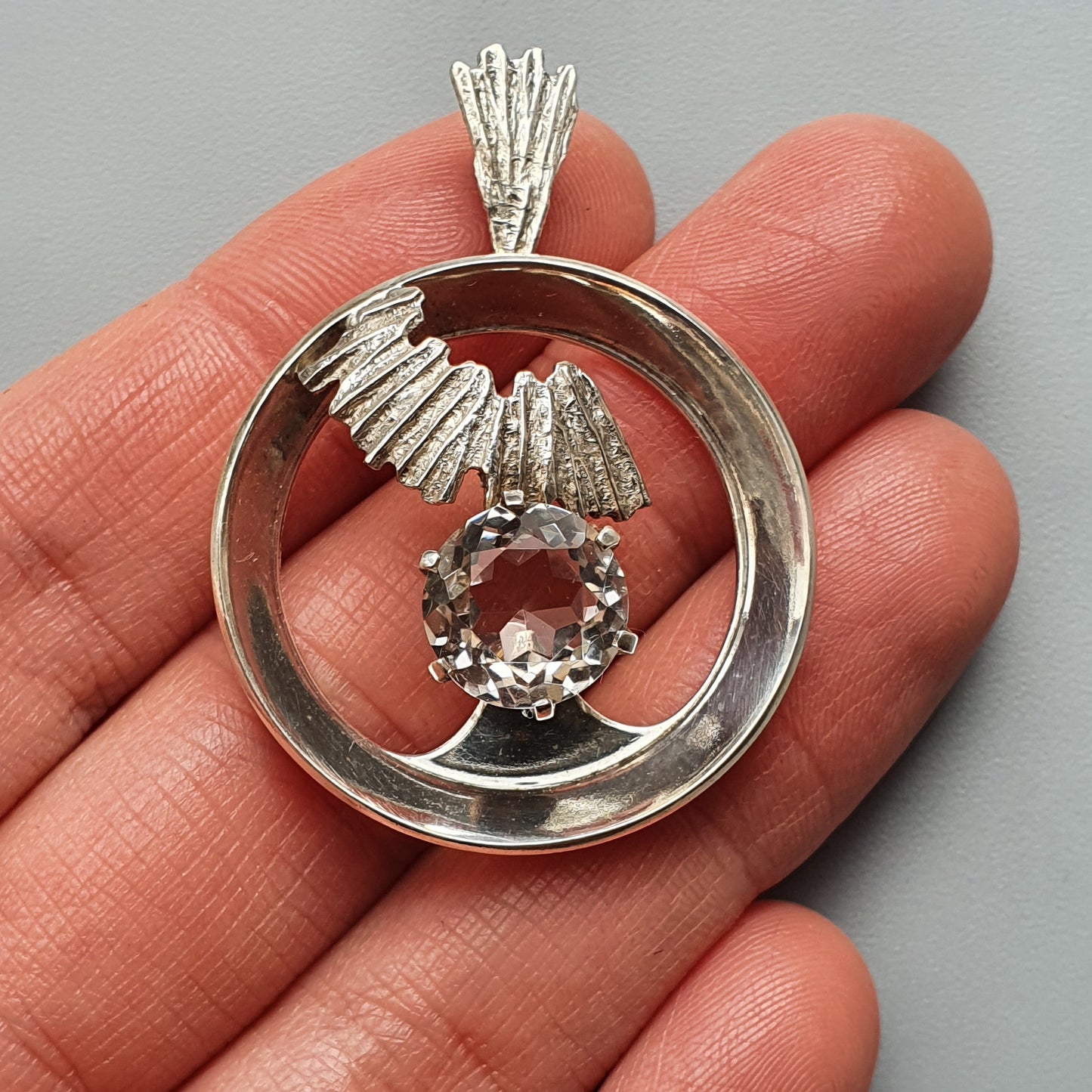 Silver pendant featuring an eagle design with a circular frame and a small gemstone.