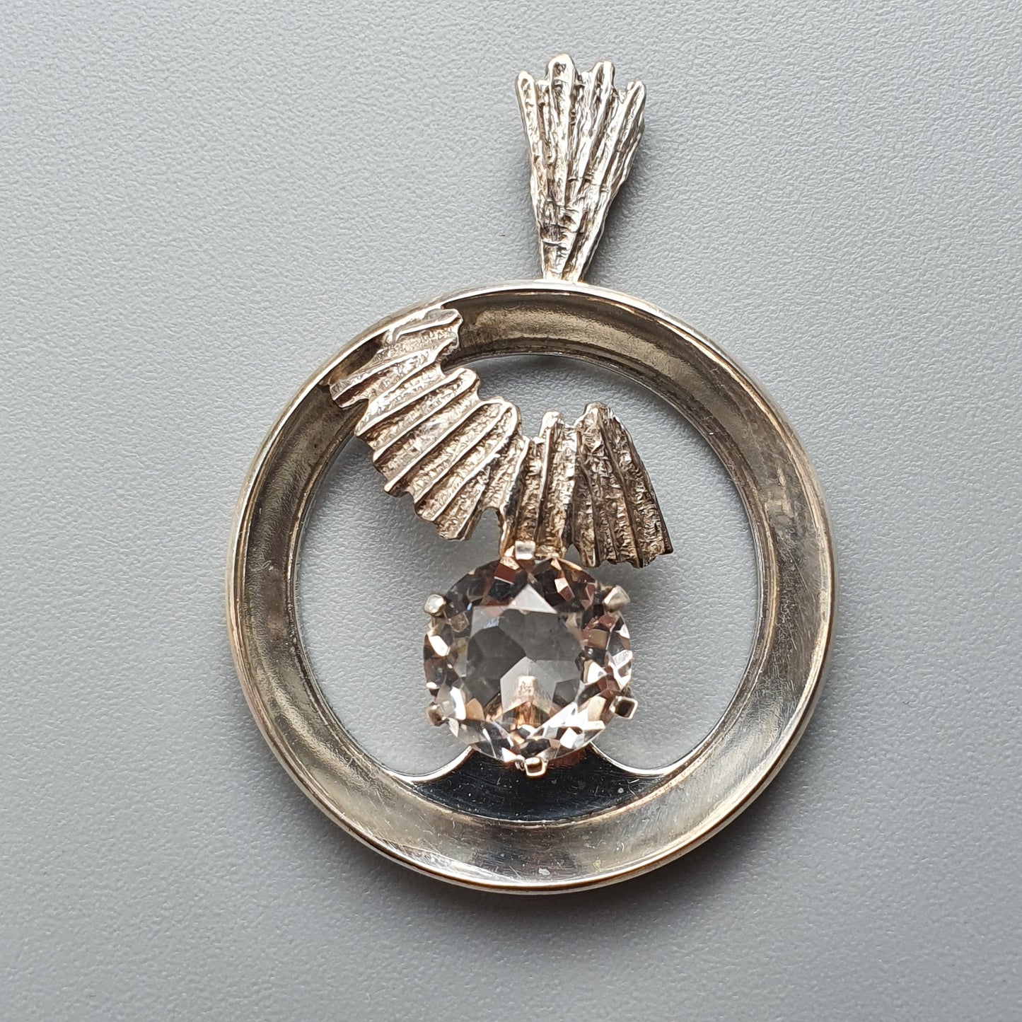 Circular silver pendant featuring a gemstone and decorative metalwork.