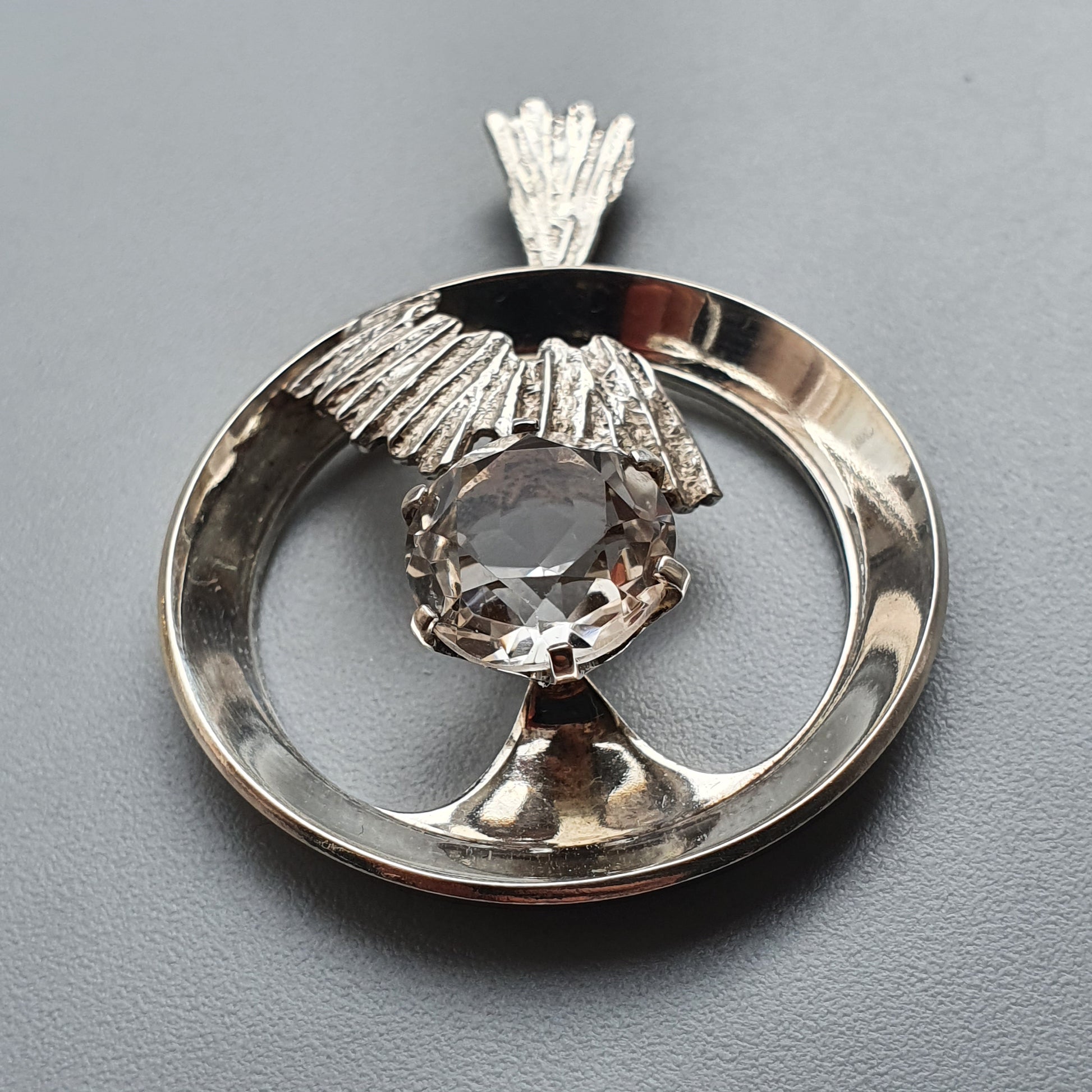 Silver pendant featuring a circular design with a central gemstone and decorative elements.