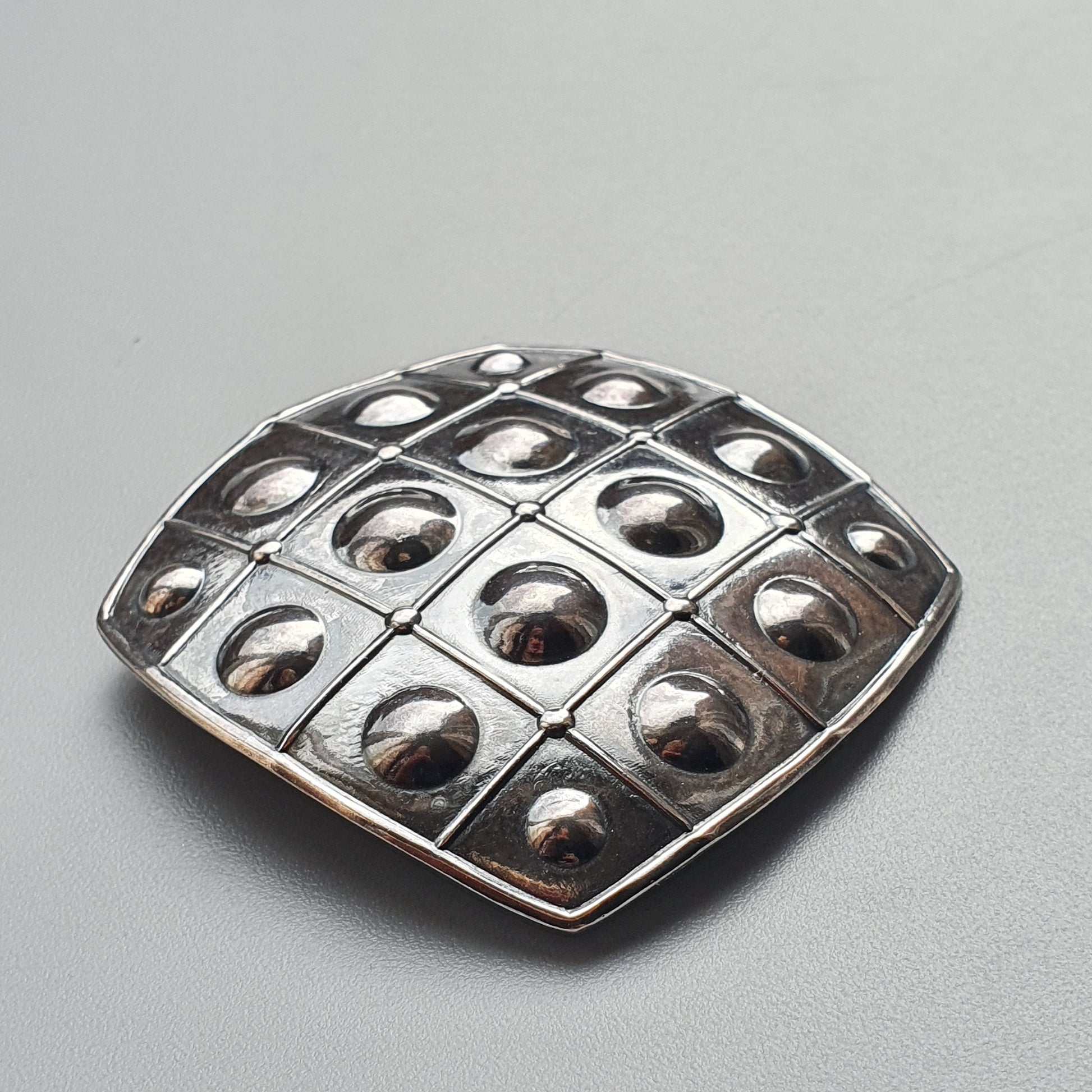 Metallic brooch or pendant with a grid pattern of raised circular domes.