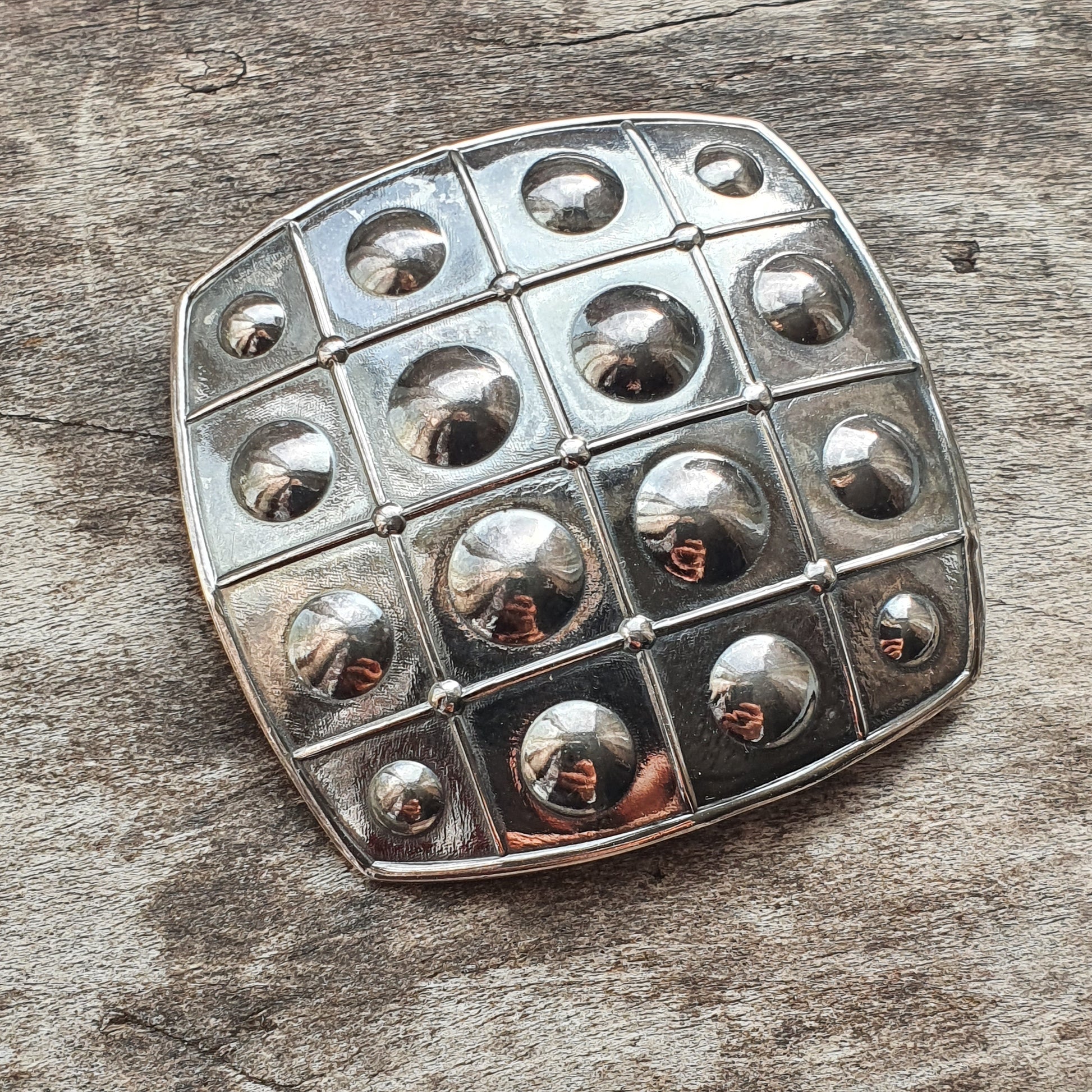 Metal grid-like object with rounded indentations arranged in a square pattern.