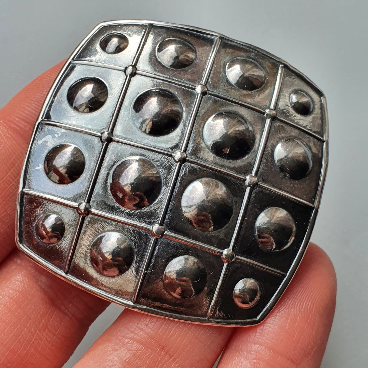 Metallic square brooch or pendant with a grid pattern of raised domes.