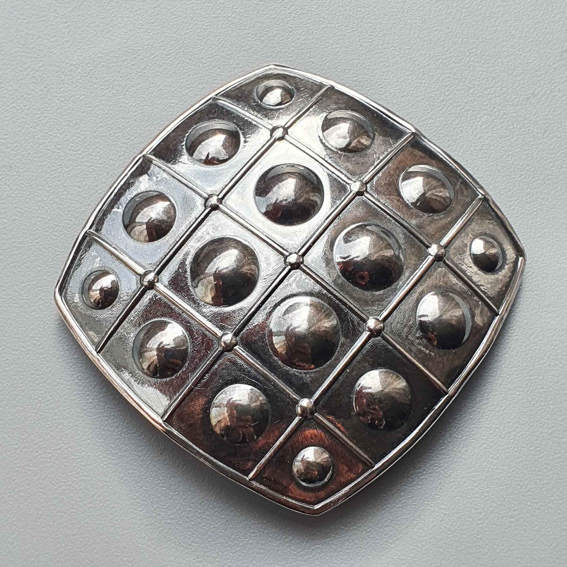 Metallic brooch or pendant with a grid pattern of raised spherical domes.