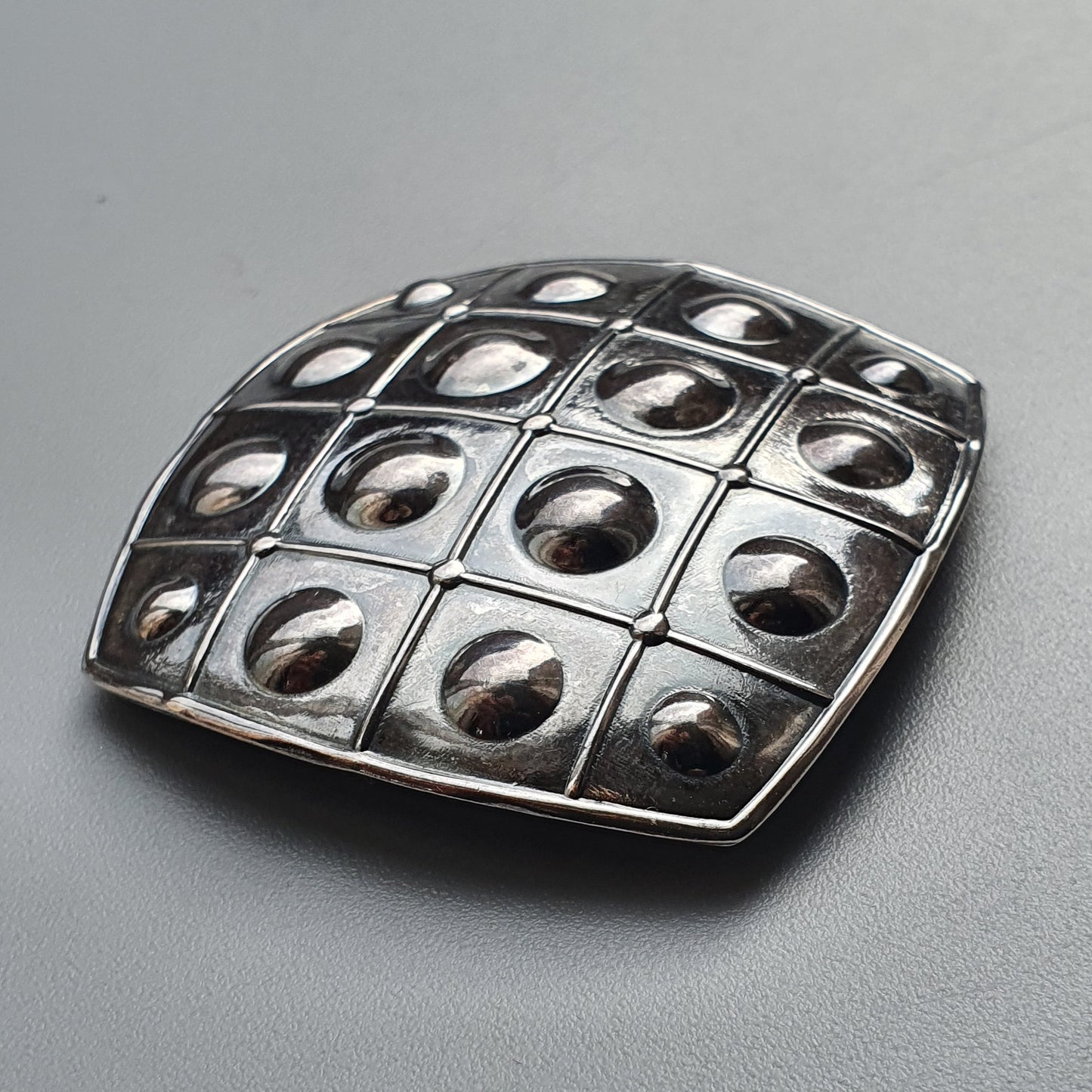 Metallic square brooch or pendant with a grid pattern of circular indentations.