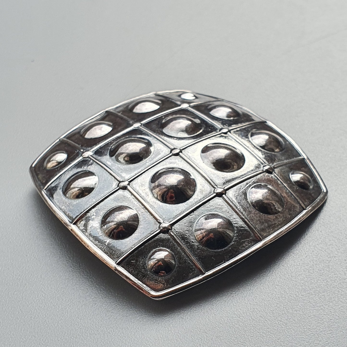 Square metallic brooch or pendant with a grid pattern of raised domes.