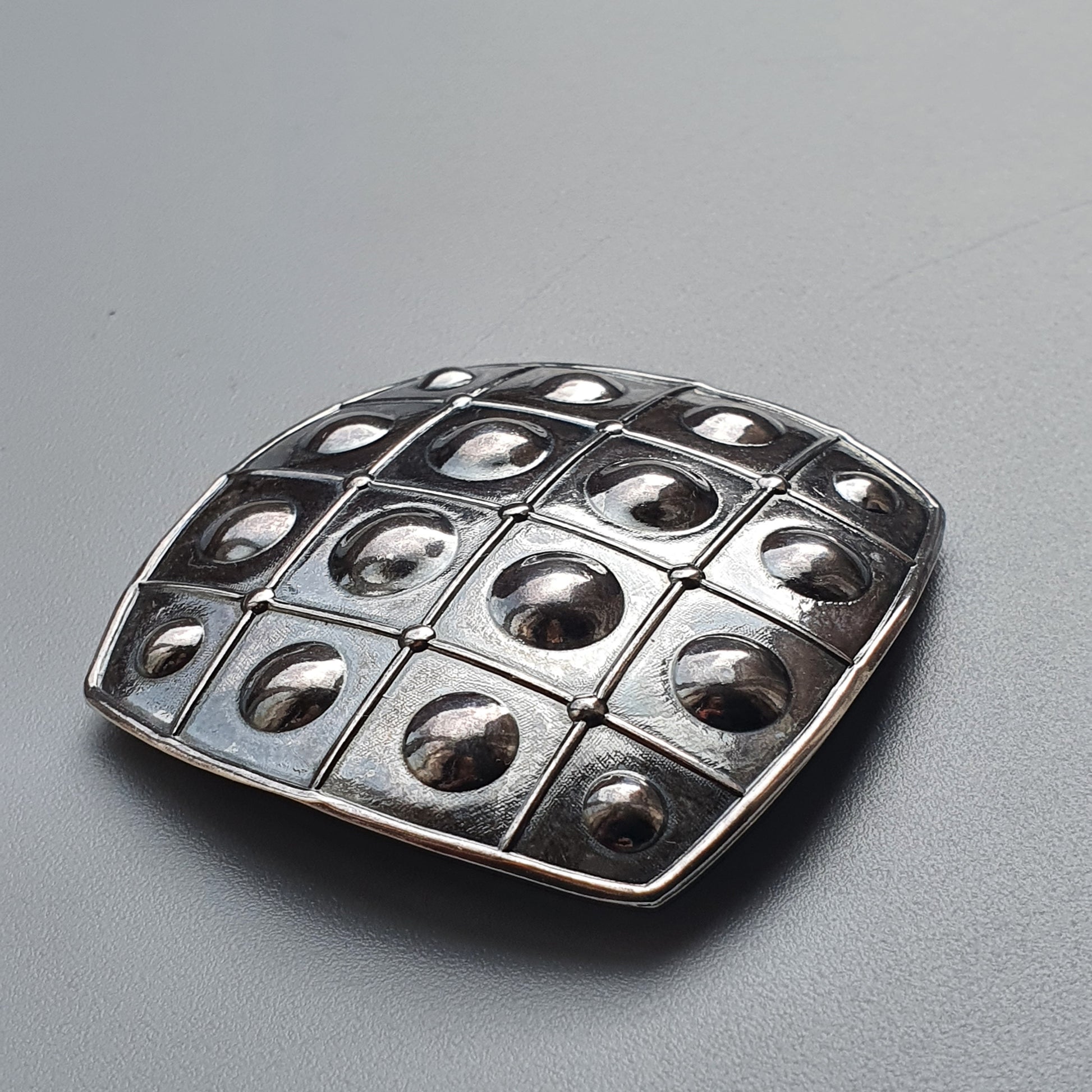 Metallic belt buckle with a grid pattern of raised domes or bubbles.