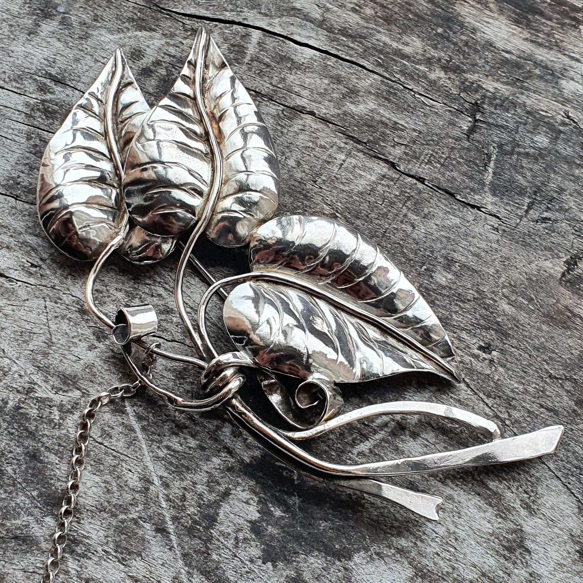 Silver leaf-shaped brooch with intricate detailing and a chain attachment.