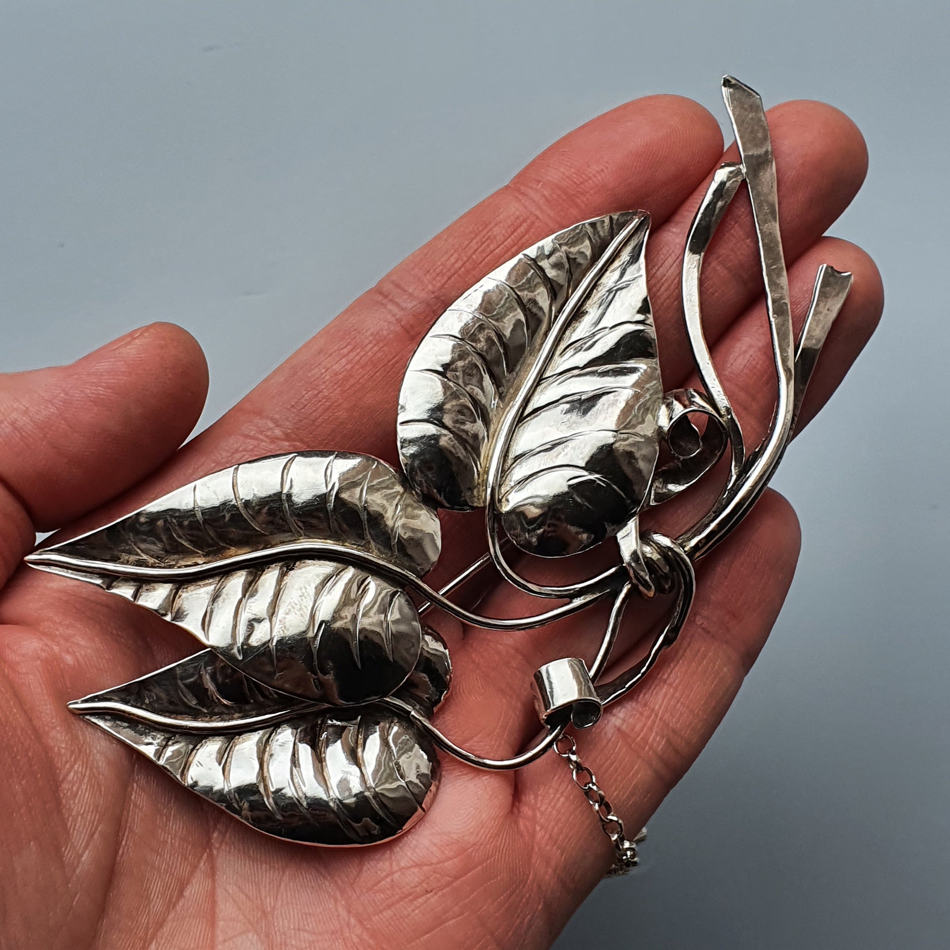 Silver leaf-shaped brooch or pendant with intricate detailing held in a person’s palm.