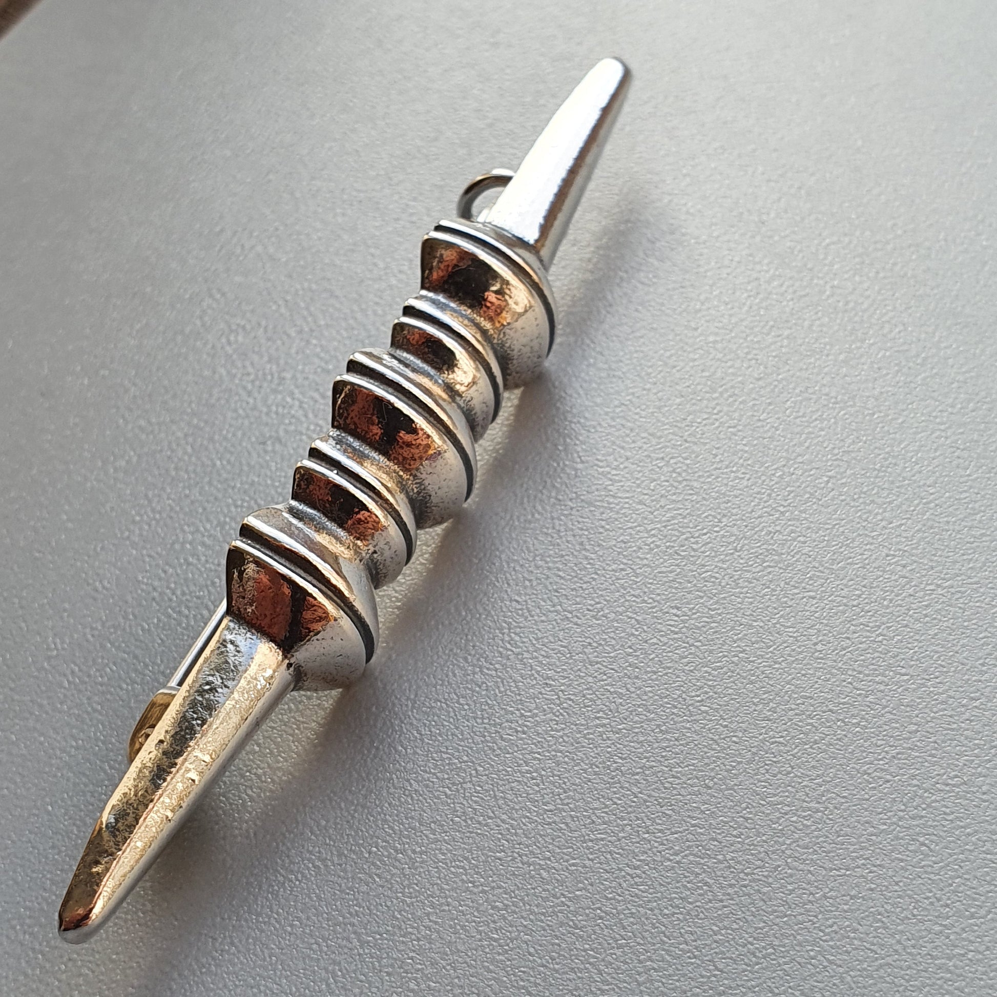 Metal spike or pin with decorative spiral grooves along its shaft.