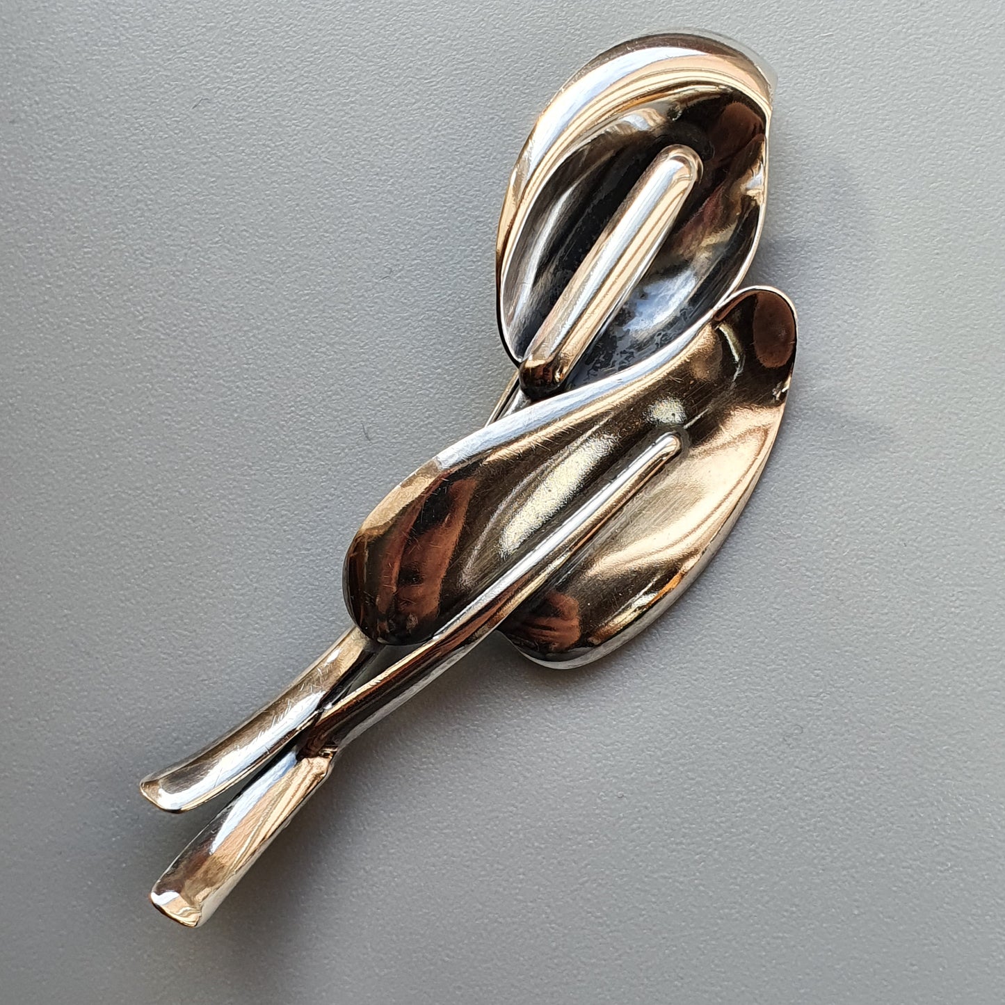 Abstract metallic brooch or pin with curved, flowing shapes resembling a stylized figure.