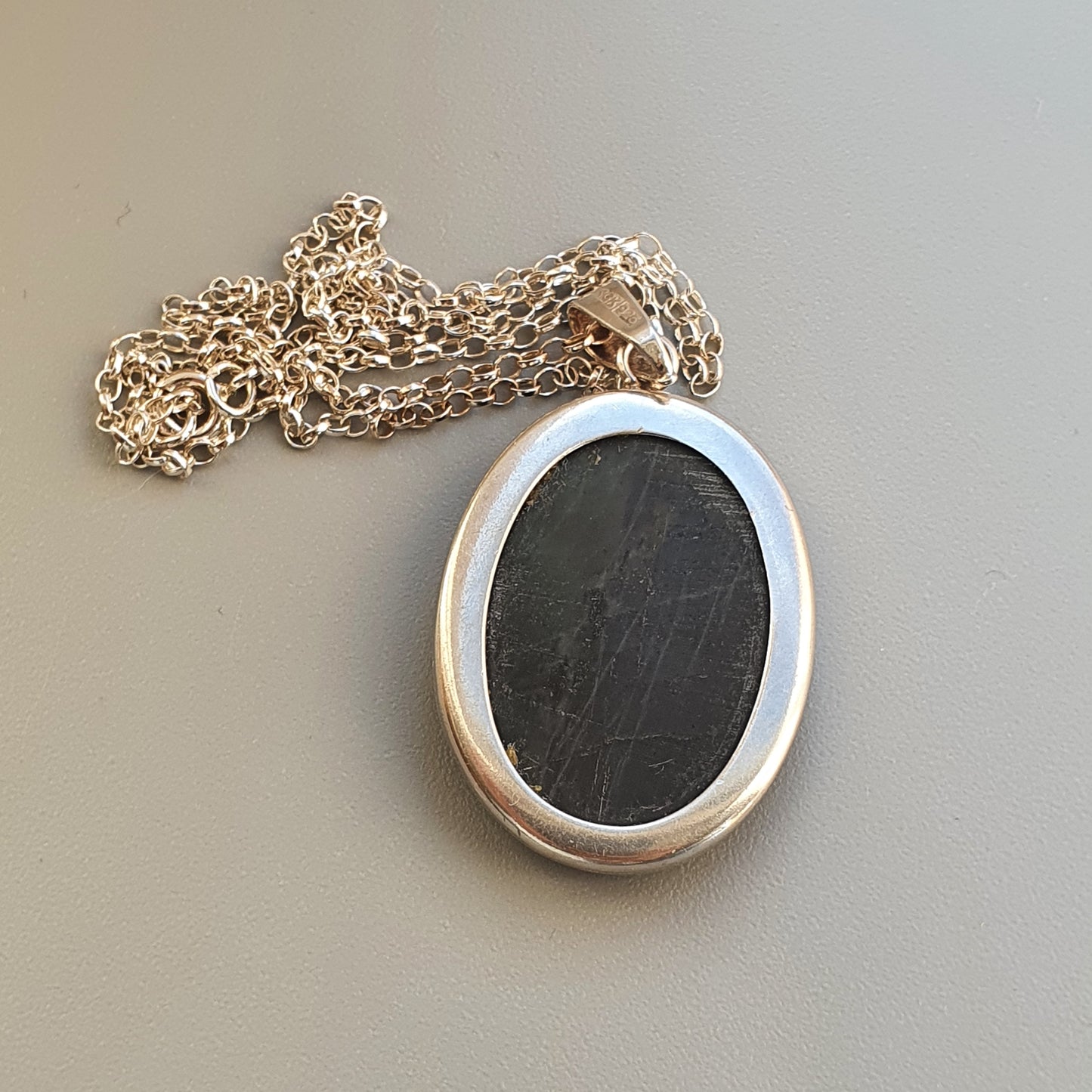 Oval silver pendant with a dark center on a chain necklace.