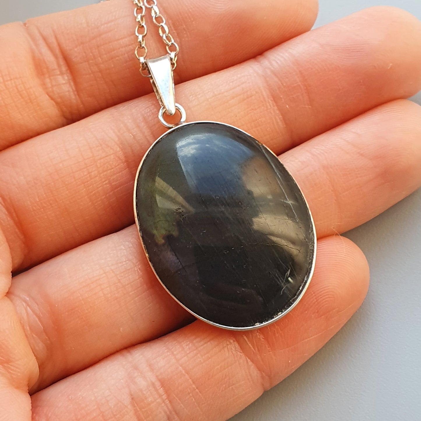 Oval pendant necklace with a dark, iridescent gemstone set in silver.