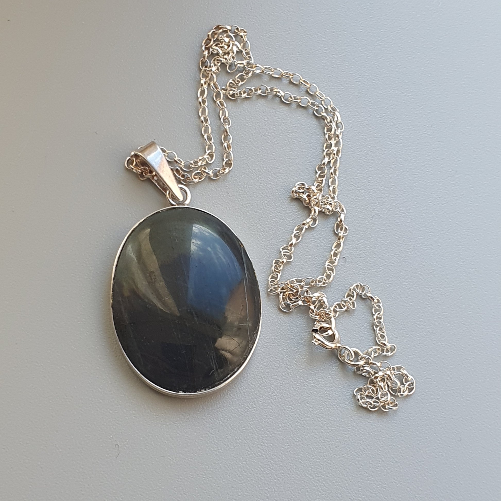 Oval pendant necklace with a dark stone set in silver.