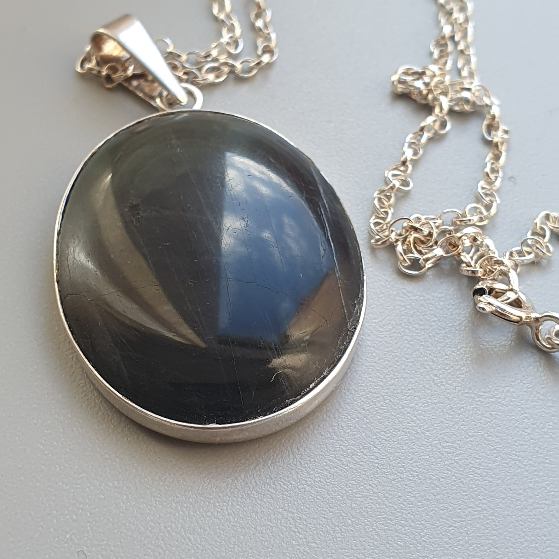 Oval pendant necklace featuring a dark, glossy stone set in silver.