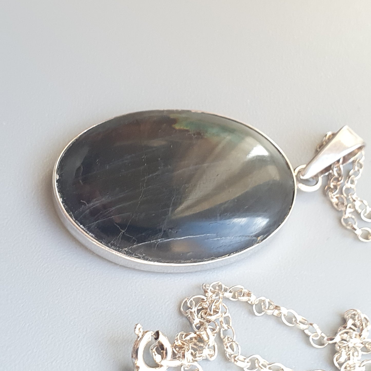 Oval-shaped pendant with a dark, reflective surface set in a silver frame attached to a chain.