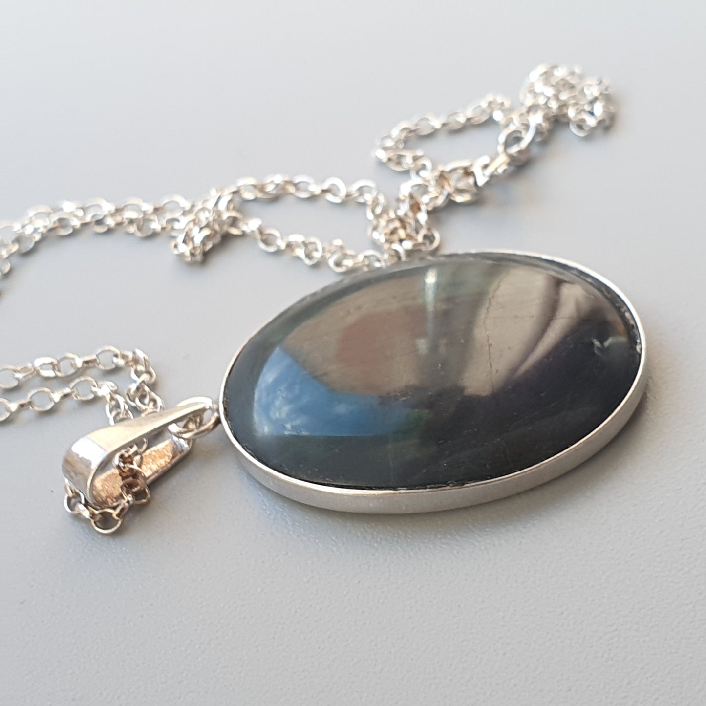 Oval pendant necklace with a dark, reflective gemstone set in silver.