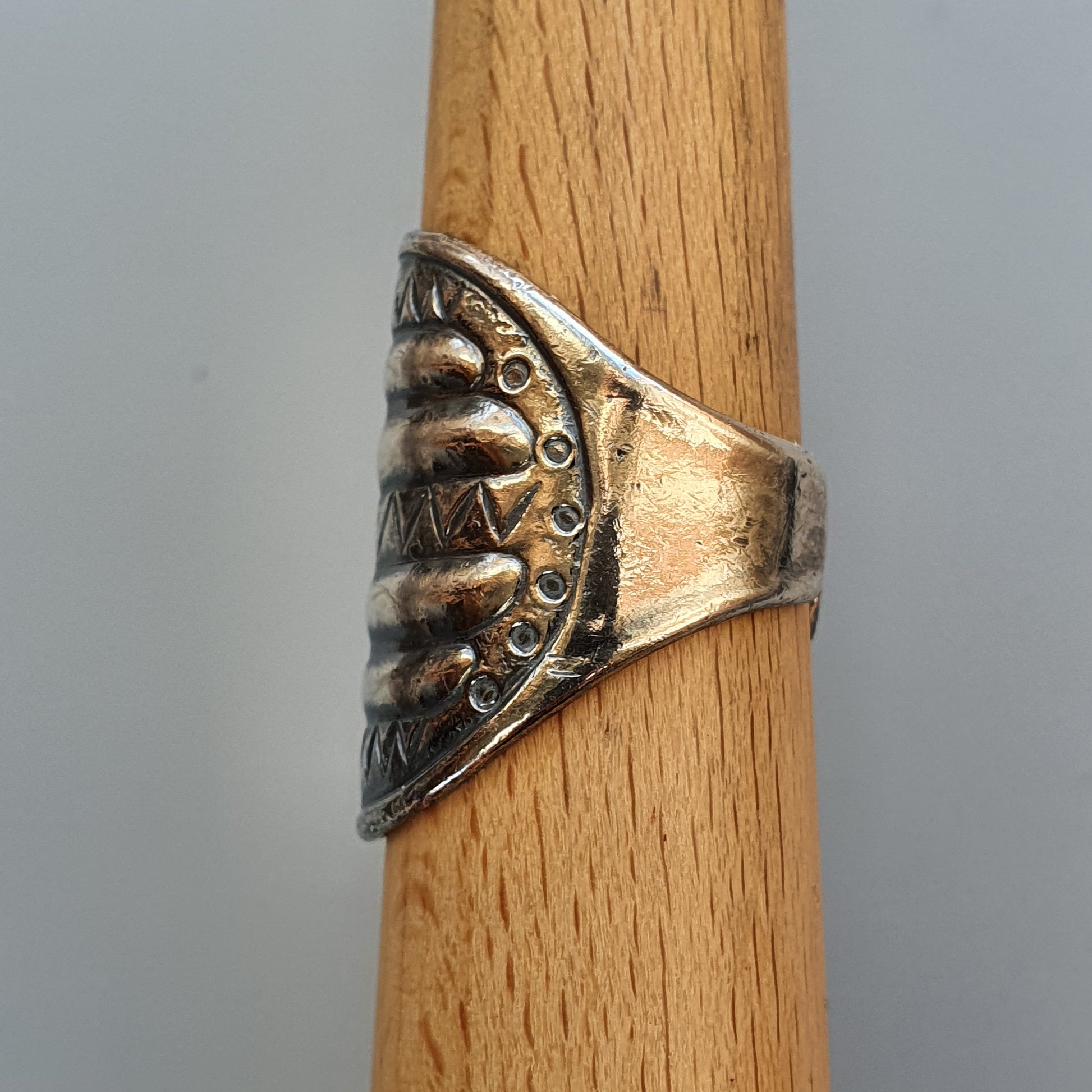 Ornate silver ring with a face-like design worn on a wooden dowel.